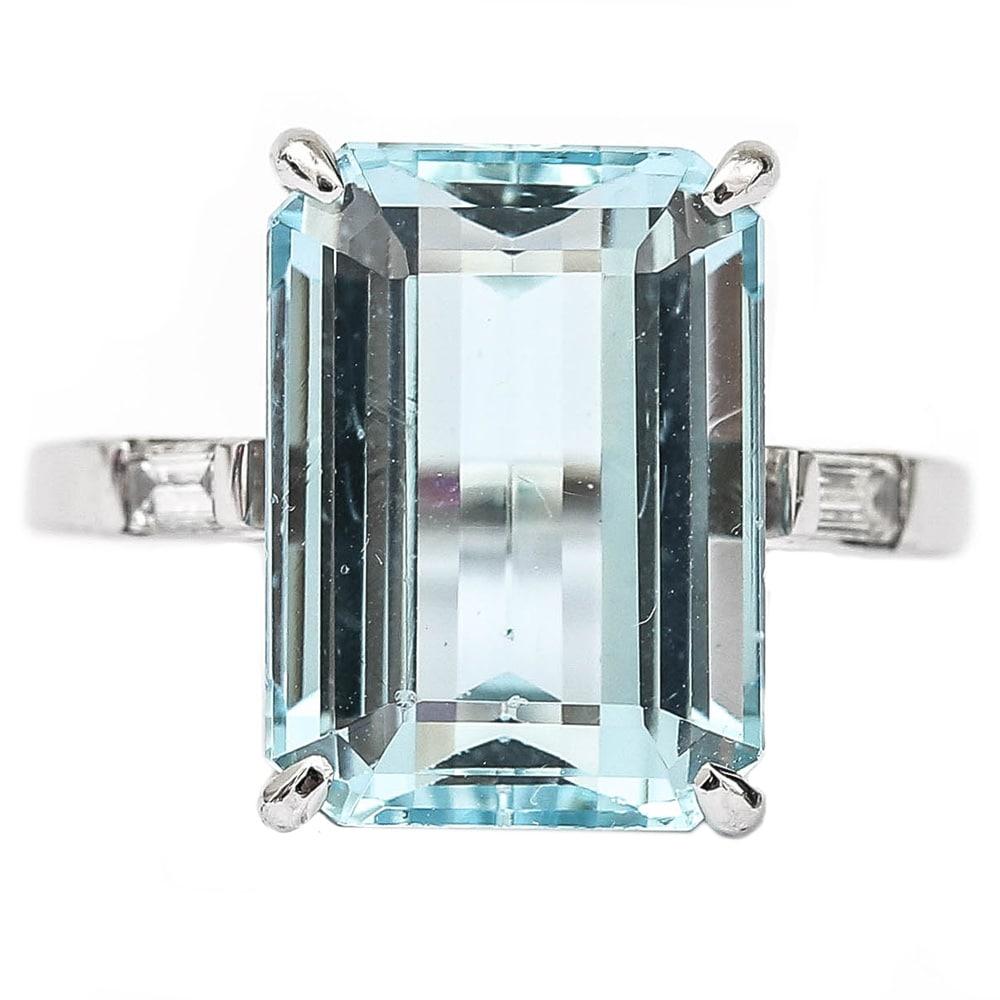 A stunning contemporary 18 karat white gold large approx 9.02 carat emerald cut aquamarine, claw set in a simple mount. Flanked on either side of the shank are two baguette diamonds each est. 0.15ct per side with a total weight of 0.30cts. This