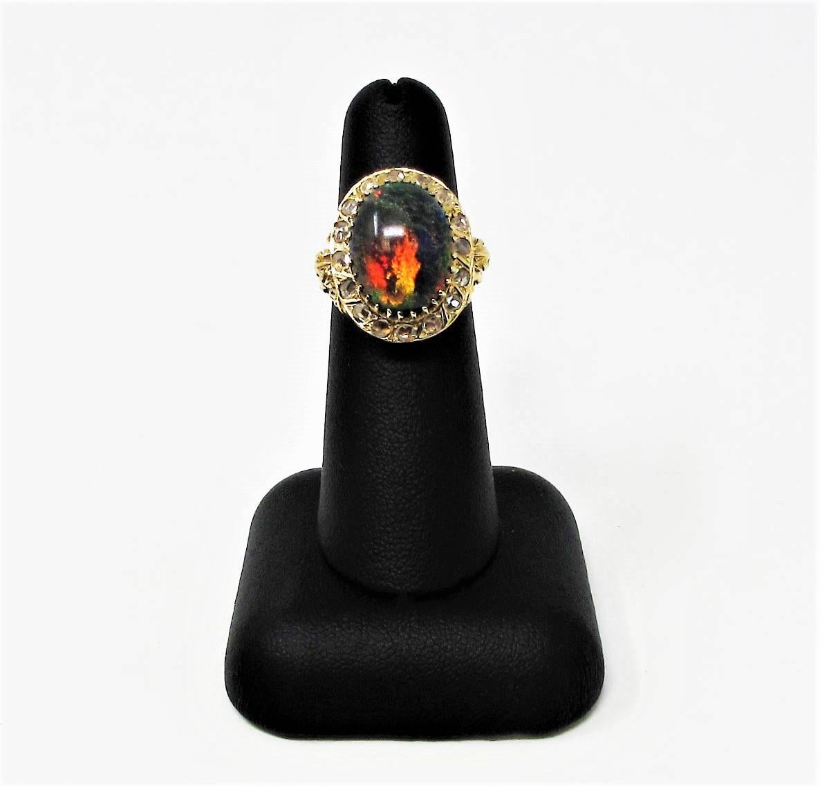 Truly incredible black opal and diamond cocktail ring with bold, vibrant colors. This rare, vintage piece is a visual showstopper with its iridescent play-of-color and sparking diamonds, while the ornately carved gold shank adds to the charm of this