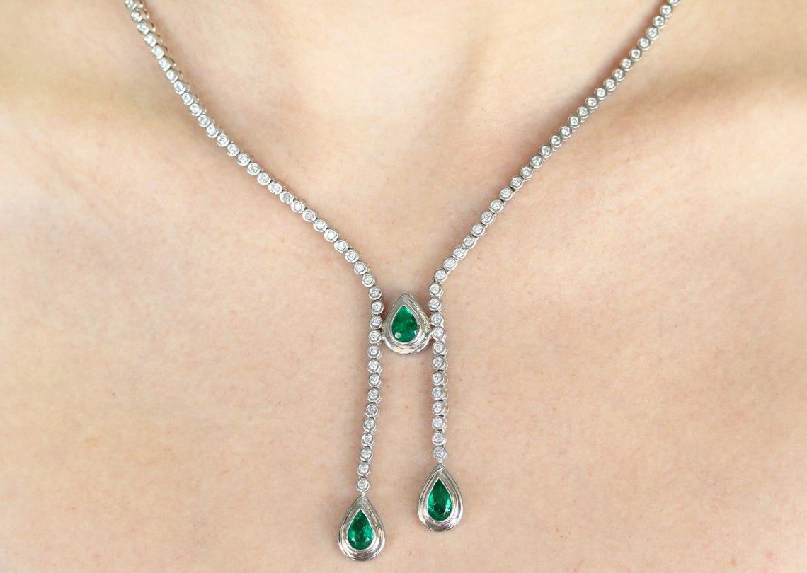 Displayed is a grand 9.24tcw emerald and diamond lariat necklace. This necklace boasts an alluring, unique design that is sure to gather compliments. Three rare, dark green Colombian emeralds weighing a total of 5.02cts and are elegantly bezel set