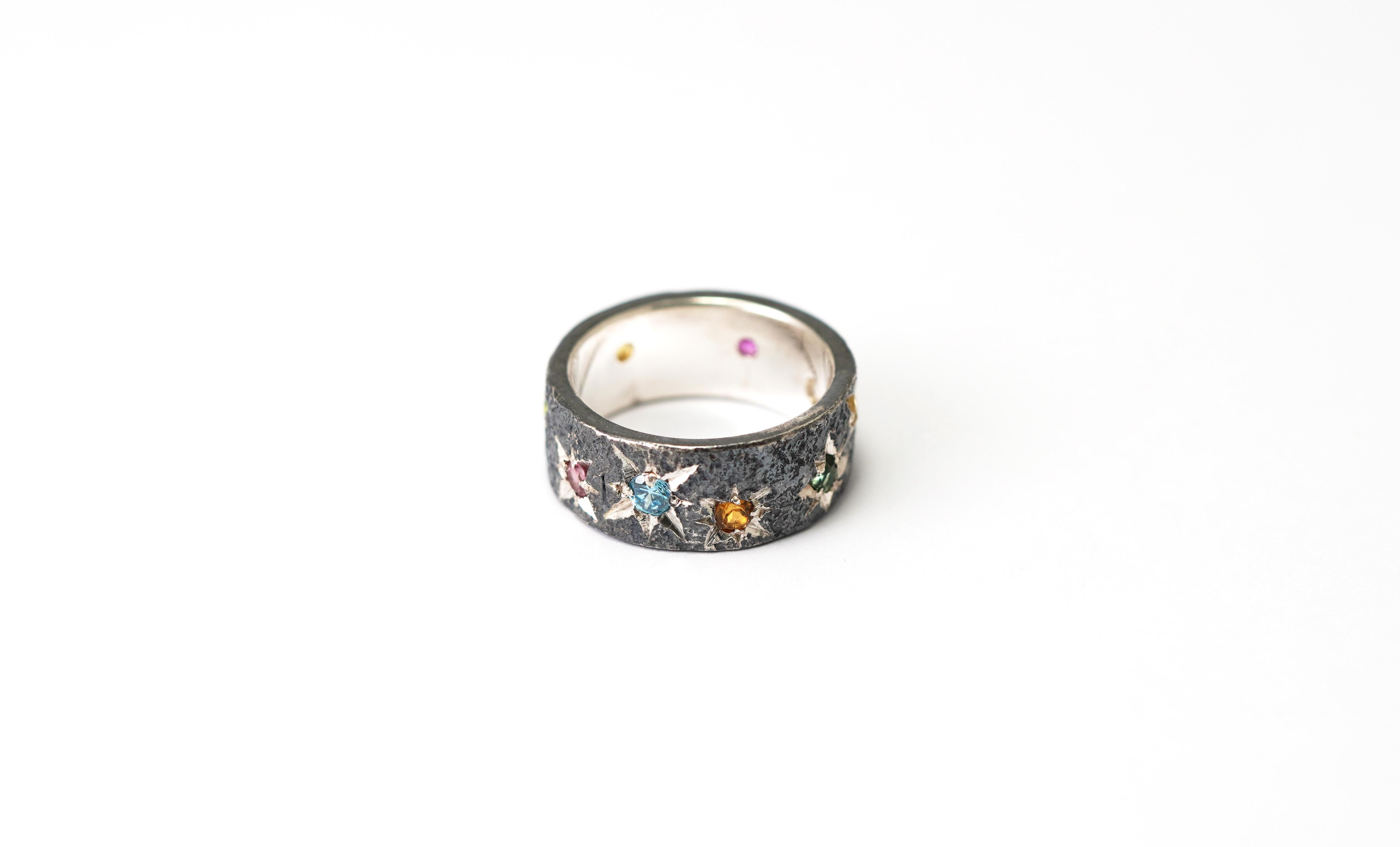 Un univers de couleurs capturé dans de l'argent oxydé.

Cette bague artisanale, forgée en argent oxydé 925, a le caractère audacieux d'un travail artisanal et la mystique d'un ciel nocturne. Sa surface texturée est parsemée de tourmalines