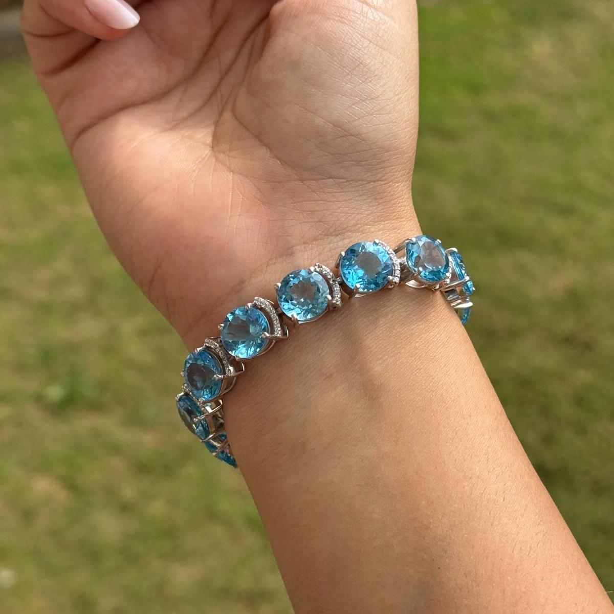 Ce bracelet de tennis en argent 925 est composé de topaze bleue naturelle et de zircon. Les pierres sont facettées de manière experte afin de maximiser leur brillance et sont rehaussées de zircon cubique étincelant pour plus de glamour. Le fermoir