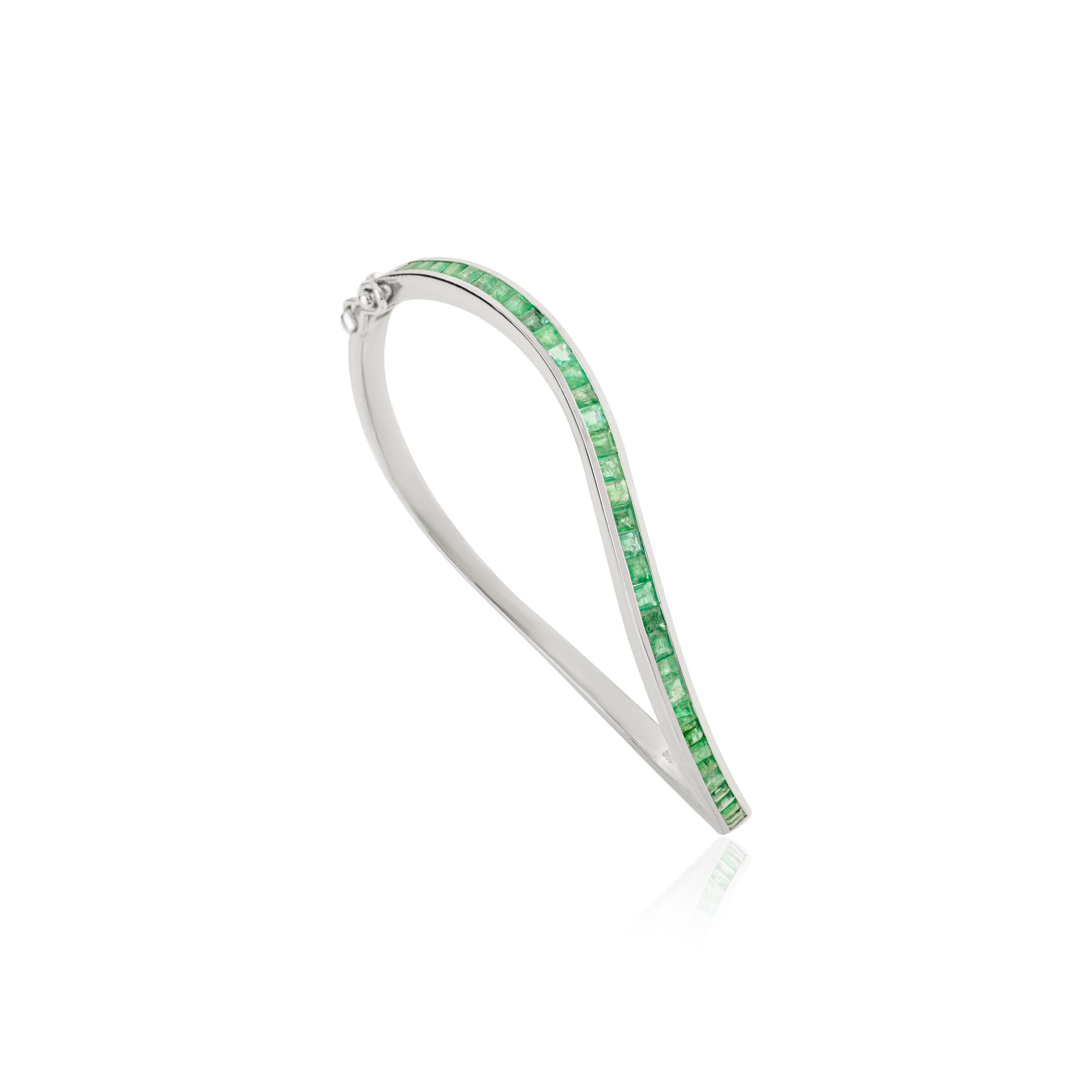 This Wave-Design 2.67Ct Natural Emerald Sleek Bangle Bracelet is a striking fusion of timeless elegance and contemporary design. Crafted in 925 sterling silver, it features a continuous line of square-cut natural emeralds, the vibrant May birthstone