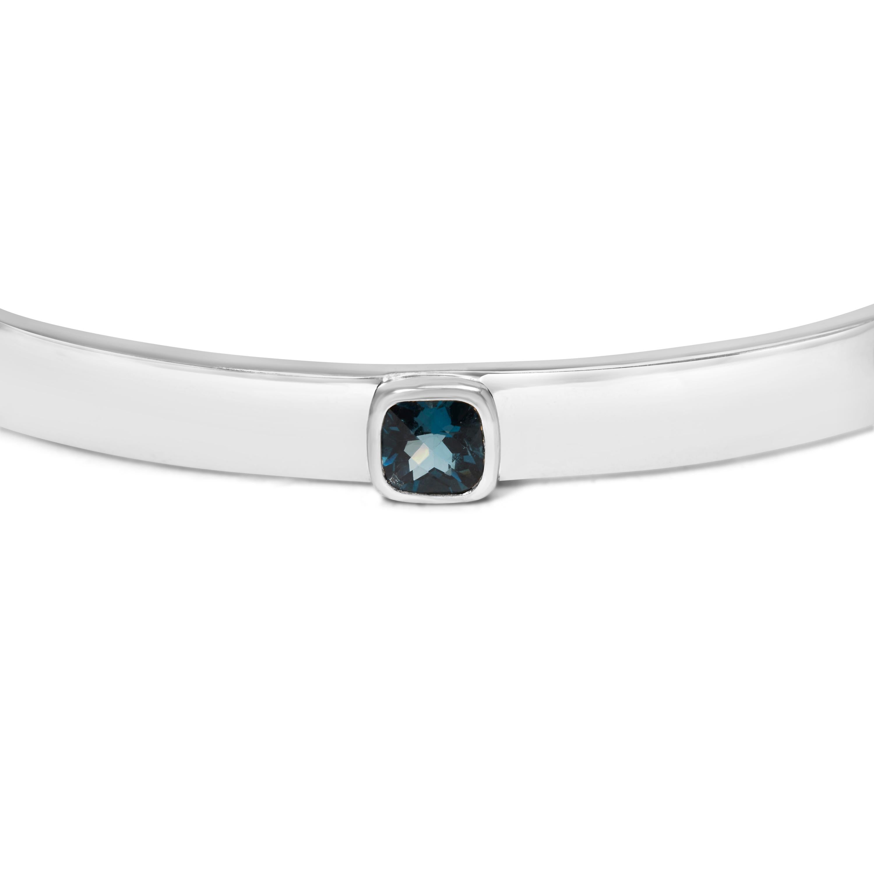 Introducing a dazzling masterpiece that will adorn your wrist with elegance and grace. This exquisite .925 Sterling Silver bangle showcases a mesmerizing 5mm Checkerboard Cushion Cut Blue Topaz gemstone, radiating a captivating blue hue. With a