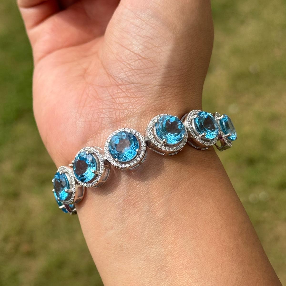 This Bolo Bracelet in Natural Blue Topaz & Zircon Jewelry striking contemporary bolo bracelet, crafted in fine 925 sterling silver. The bracelet features a dazzling array of oval-cut sky blue topaz gemstones, each set in a delicate halo of