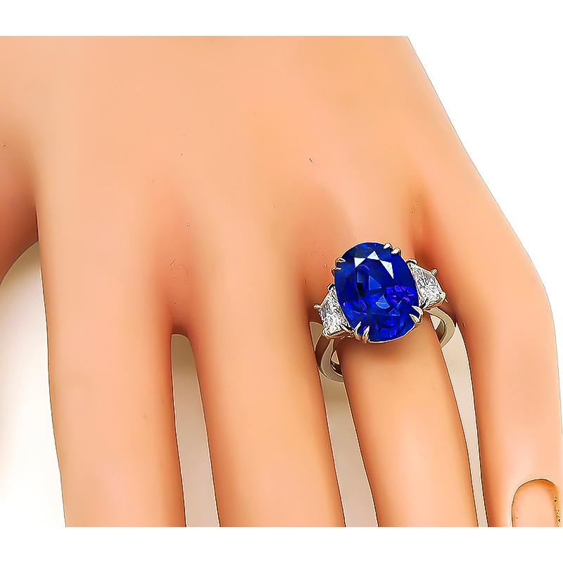 This is an elegant platinum engagement ring. The ring is centered with a lovely oval cut sapphire that weighs approximately 9.29ct. The sapphire is accentuated by sparkling trapezoid cut diamonds that weigh approximately 1.20ct. The color of these