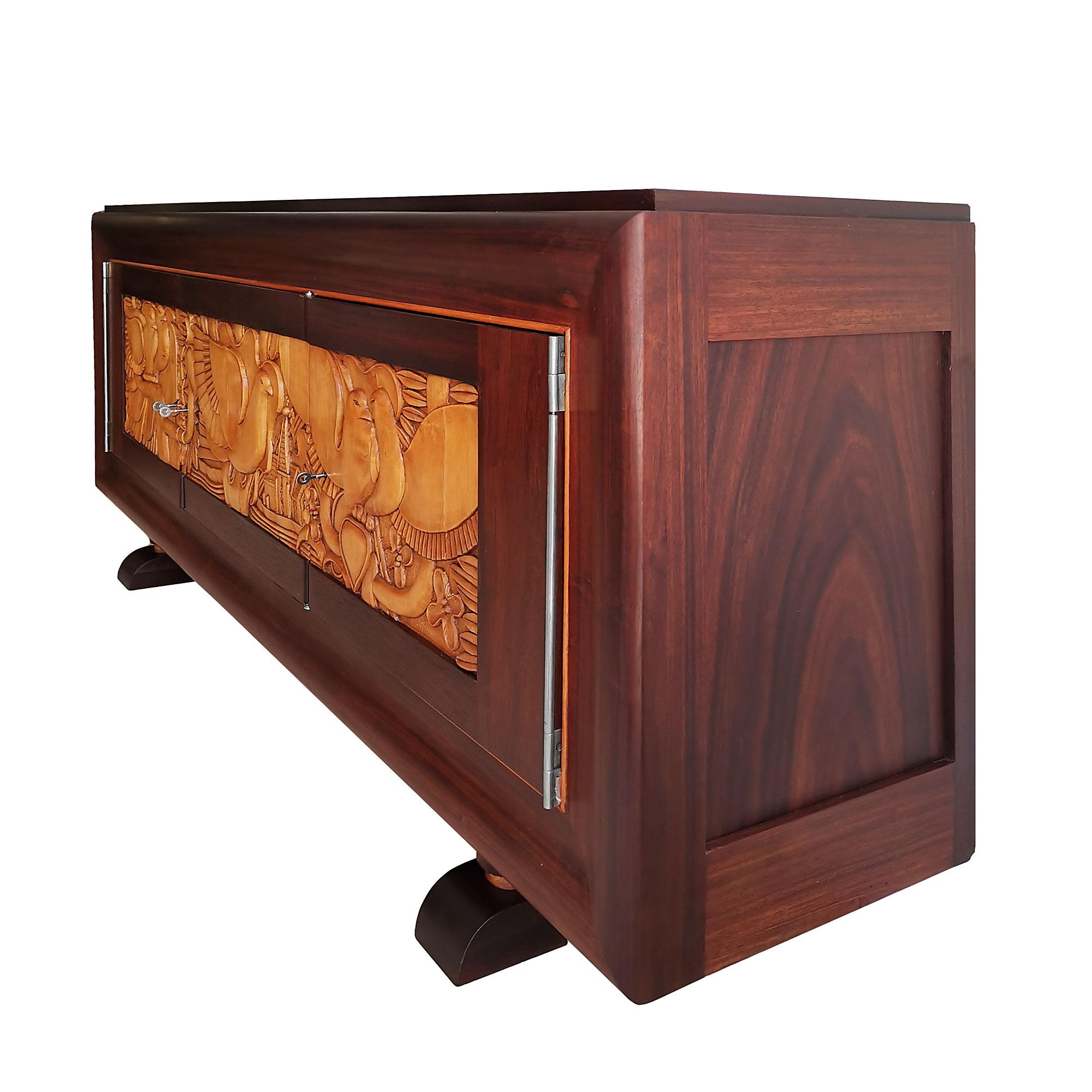 Sideboard with three doors, solid bubinga with bubinga veneer. Doors decoration in carved maple with doves, church tower and vegetal patterns. Three drawers in the central compartment and bubinga shelves on the side ones. Nickel plated bronze