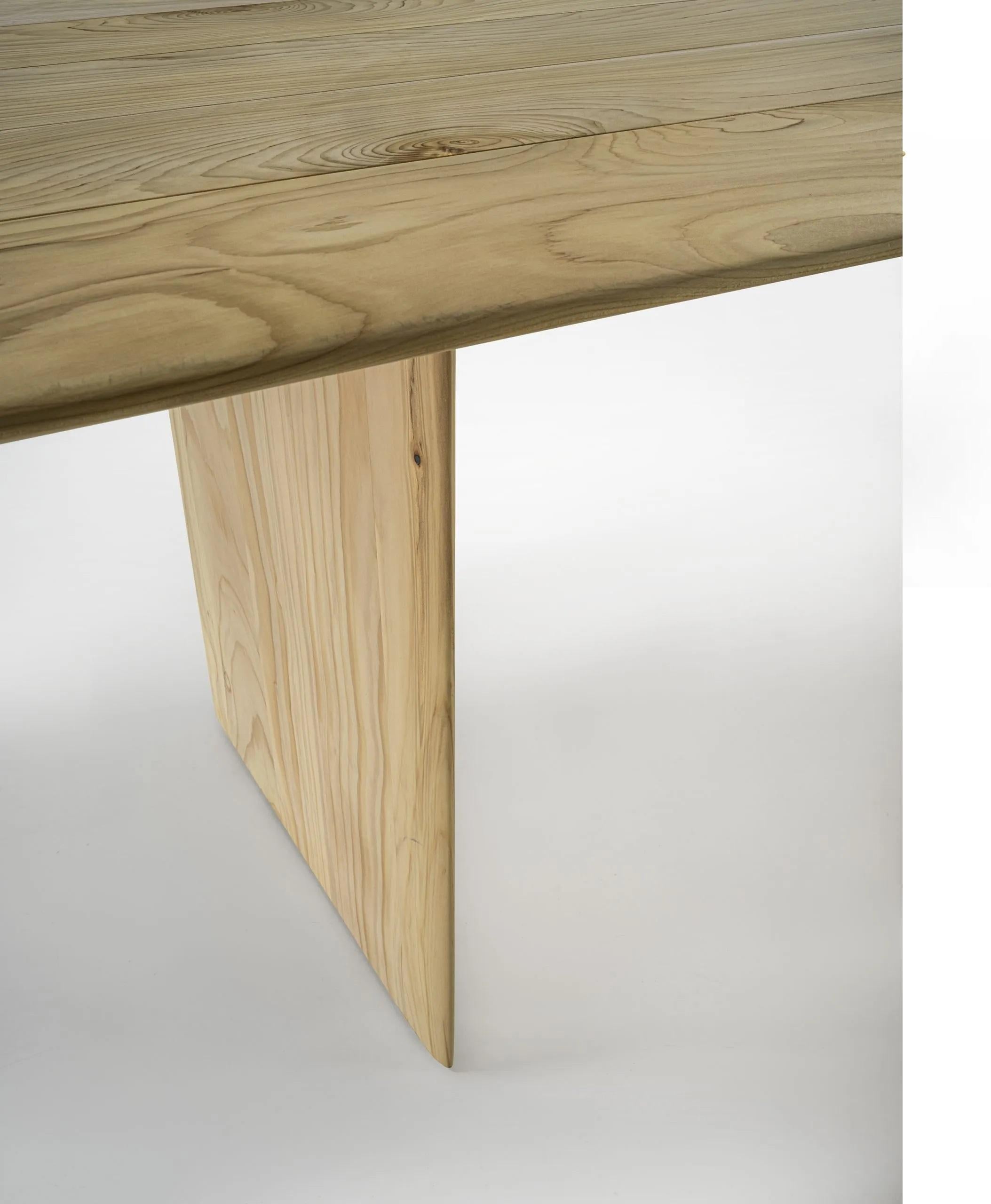 La table est entièrement fabriquée en bois de cèdre massif parfumé, avec des côtés lisses et arrondis. Son plateau et ses pieds ont une apparence élancée grâce aux bords biseautés et arrondis, ce qui lui confère un design gracieux et fluide. Le