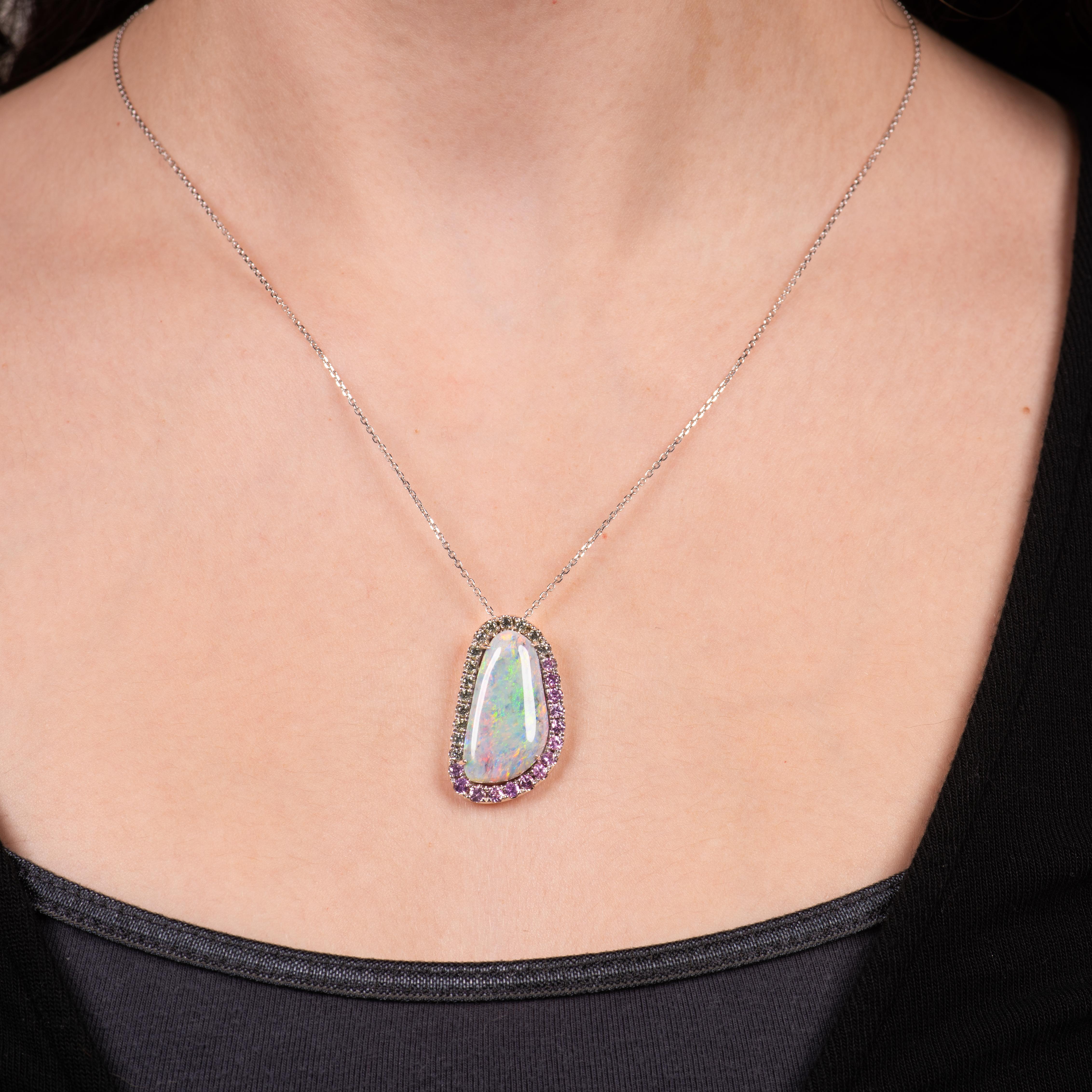 This unique necklace is a 9.45ct Australian grey opal set in 18kt white gold with a halo of 0.60ct total weight round pink sapphires and 0.60ctw in round green sapphires. There is a hidden bail.