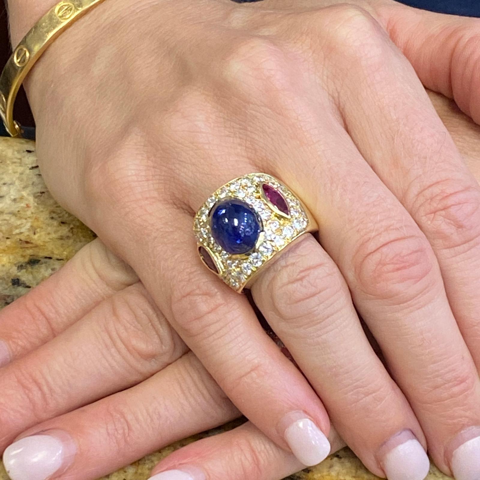Fabulous Ceylon blue sapphire, ruby, and diamond band fashioned in 18 karat yellow gold. The cabochon natural blue Ceylon sapphire weighs approximately 9.50 carats, and is certified by the AGL. The 52 round brilliant cut diamonds weigh approximately