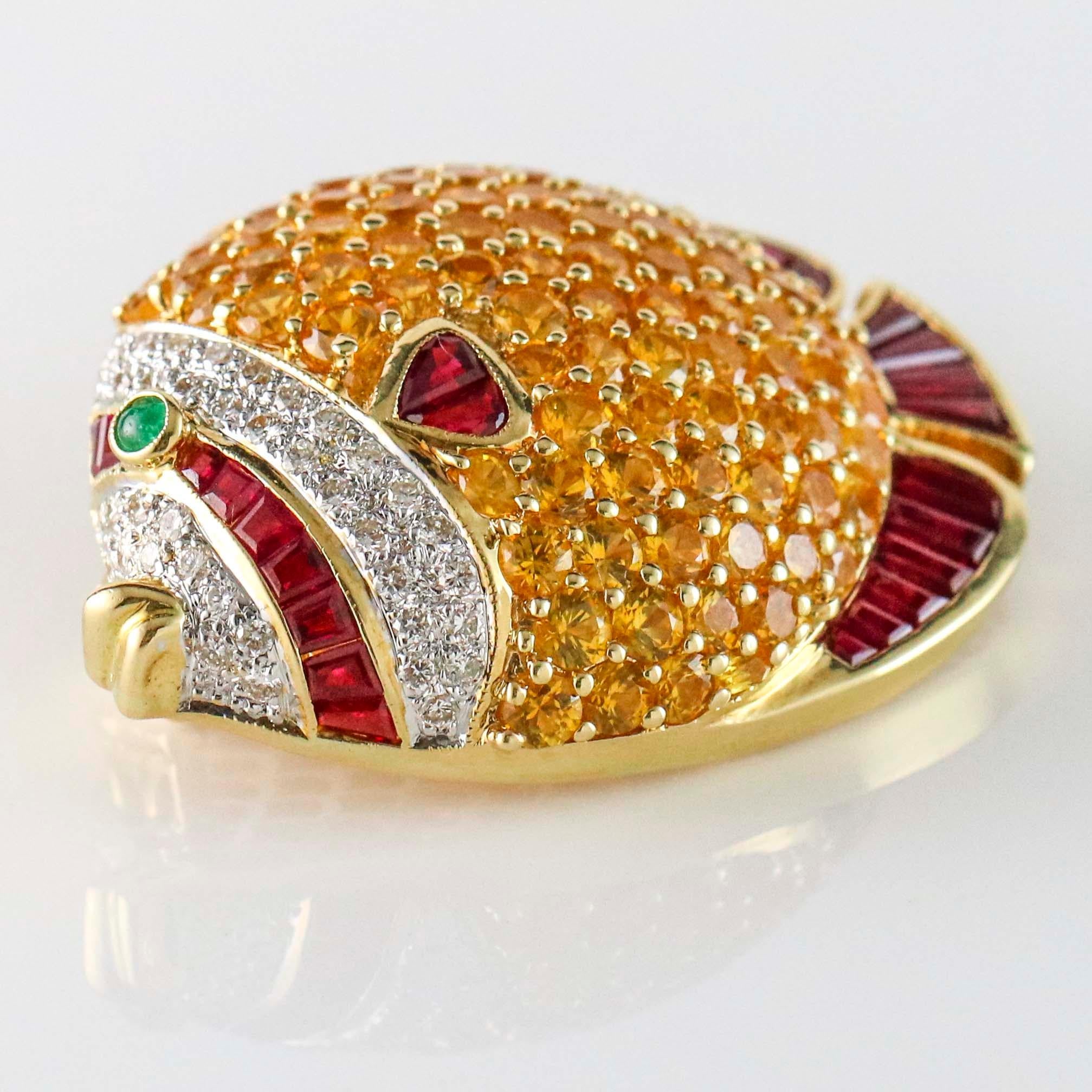 Fish pin crafted in 18k yellow gold with 7 carats of prong set natural yellow sapphires, 2 carats of channel set baguette cut rubies, .50 carats of round brilliant cut diamonds, and a bezel-set cabochon cut emerald accent on eye. 