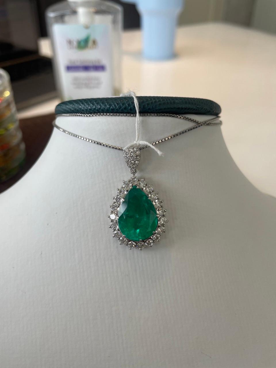 This exquisite pendant is a true masterpiece, showcasing a breathtaking pear-shaped emerald weighing an impressive 9.55 carats, with a vivid green hue that radiates luxury and timeless beauty. The emerald is encircled by a shimmering halo of round