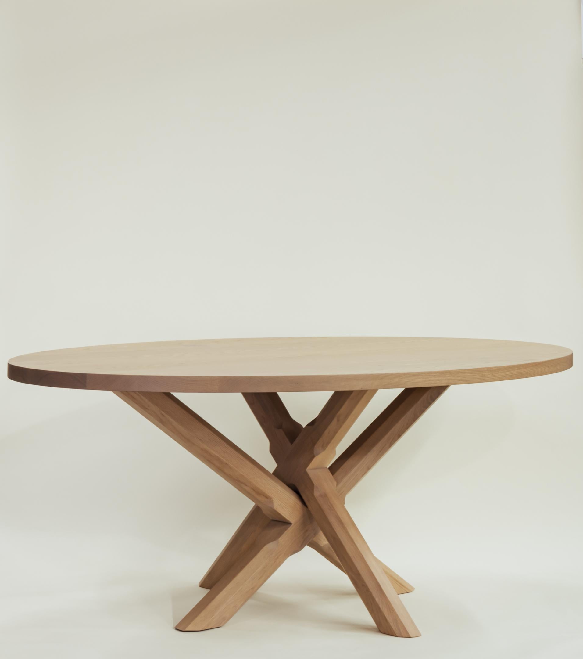 Ce guéridon ovale compact et moderne est construit entièrement en bois dur. Le plateau épais de la table repose sur une base en forme de X avec des pieds polygonaux sculptés de manière complexe. Les pieds sont composés de deux éléments distincts, ce