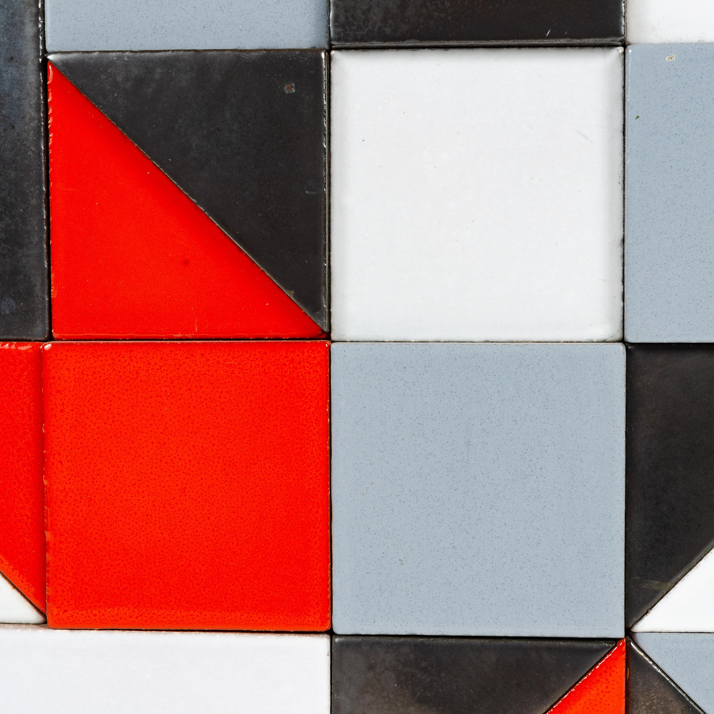 A unique constructivist artwork, comprised of an asymmetrical arrangement of black, white, grey and red-orange ceramic tiles of varying shapes and thicknesses.