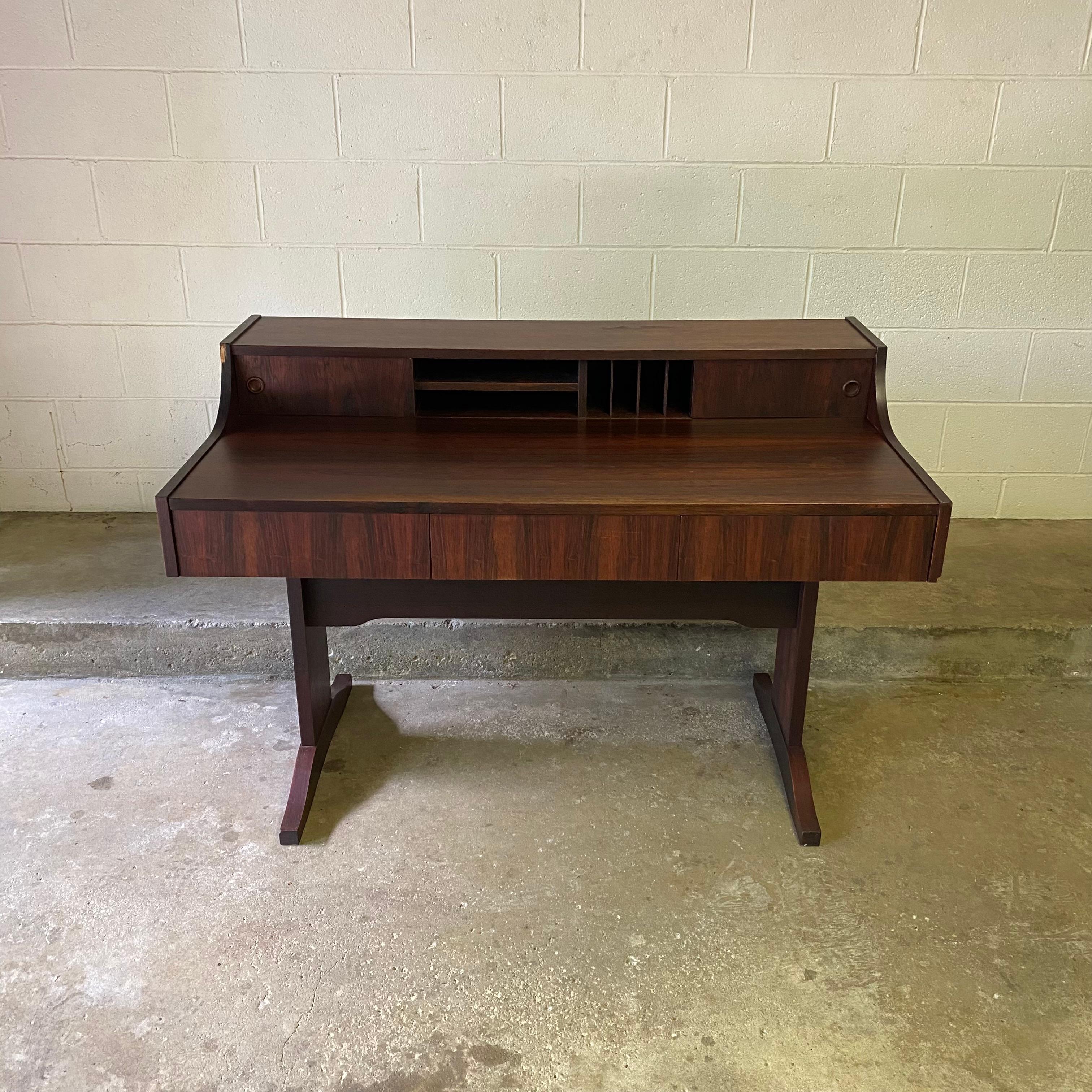 This is a stunning Danish modern rosewood desk with plenty of space for storage and work. There are three large drawers that pull out from the front as well as two sliding doors with finger hole pulls that reveal cubbies.

Condition: this desk is in