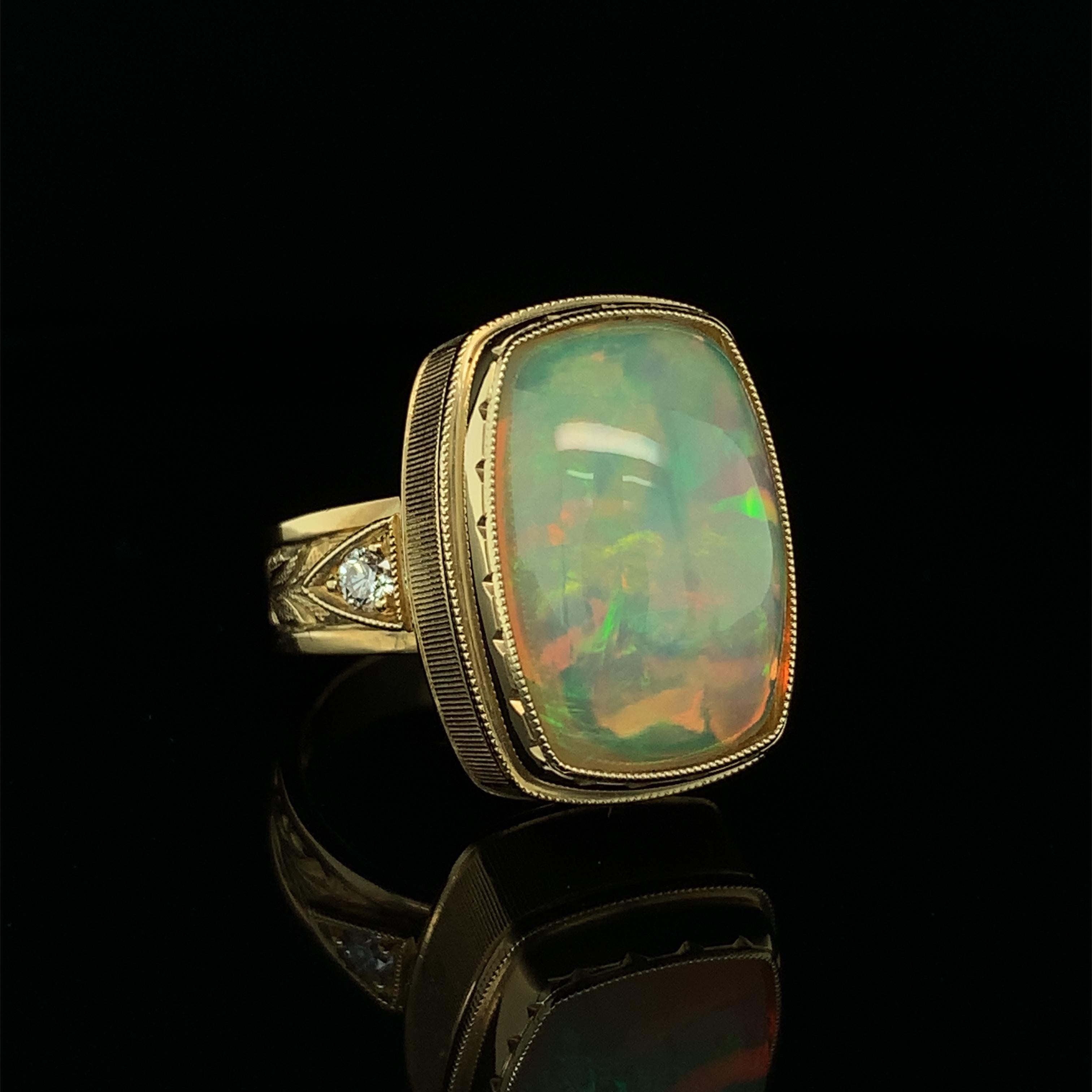 A beautiful cushion-shaped Ethiopian opal weighing 9.62 carats is featured in this handmade 18k yellow gold ring. Set in an intricately engraved bezel with 2 round brilliant diamonds, this opal comes to life with bright flashes of green, orange,