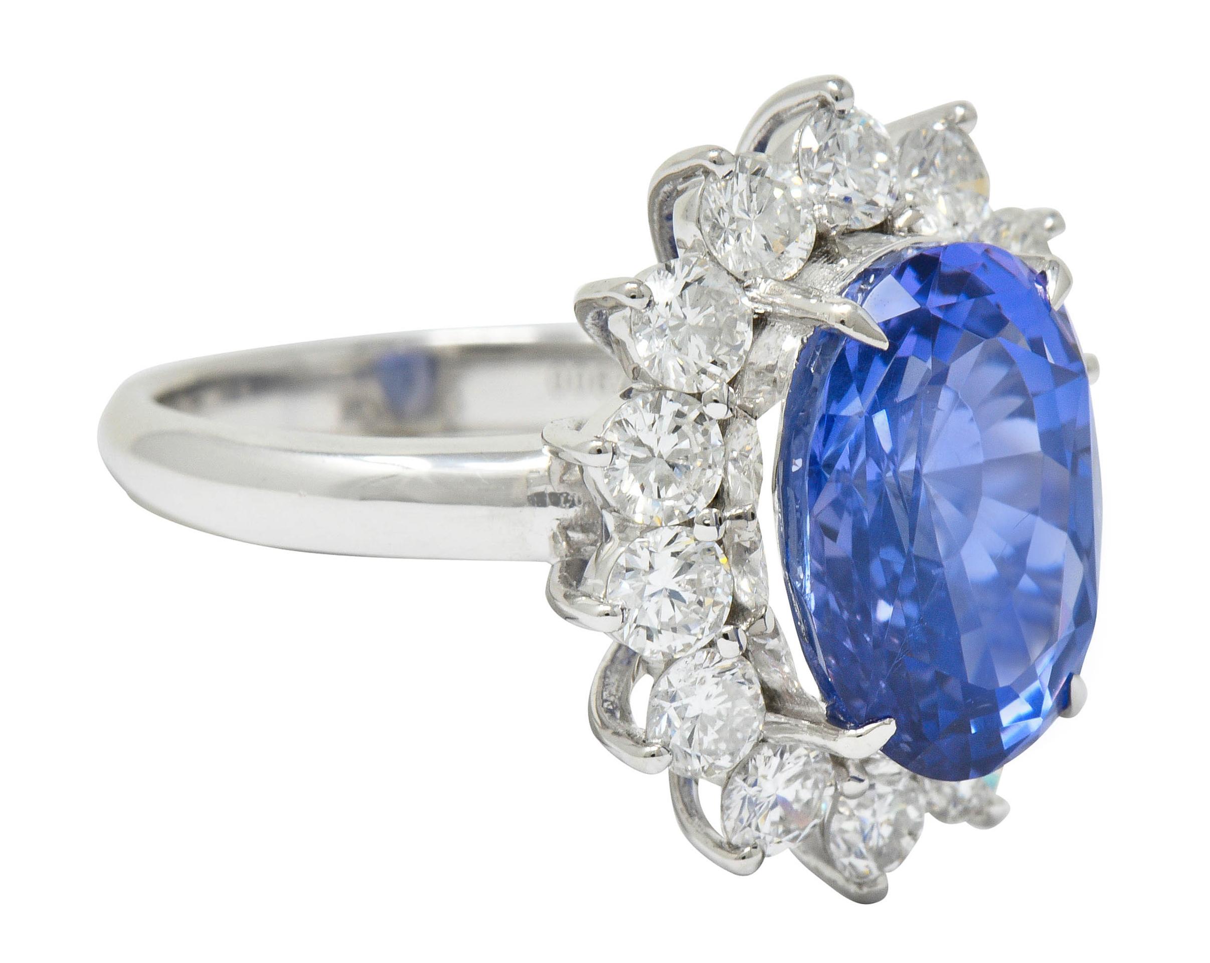 Cluster style ring centers an oval cut Ceylon sapphire weighing 7.72 carats

Cornflower blue in color with no indications of heat and is Sri Lankan in origin

Surrounded by round brilliant cut diamonds weighing in total 1.91 carats; F/G color with