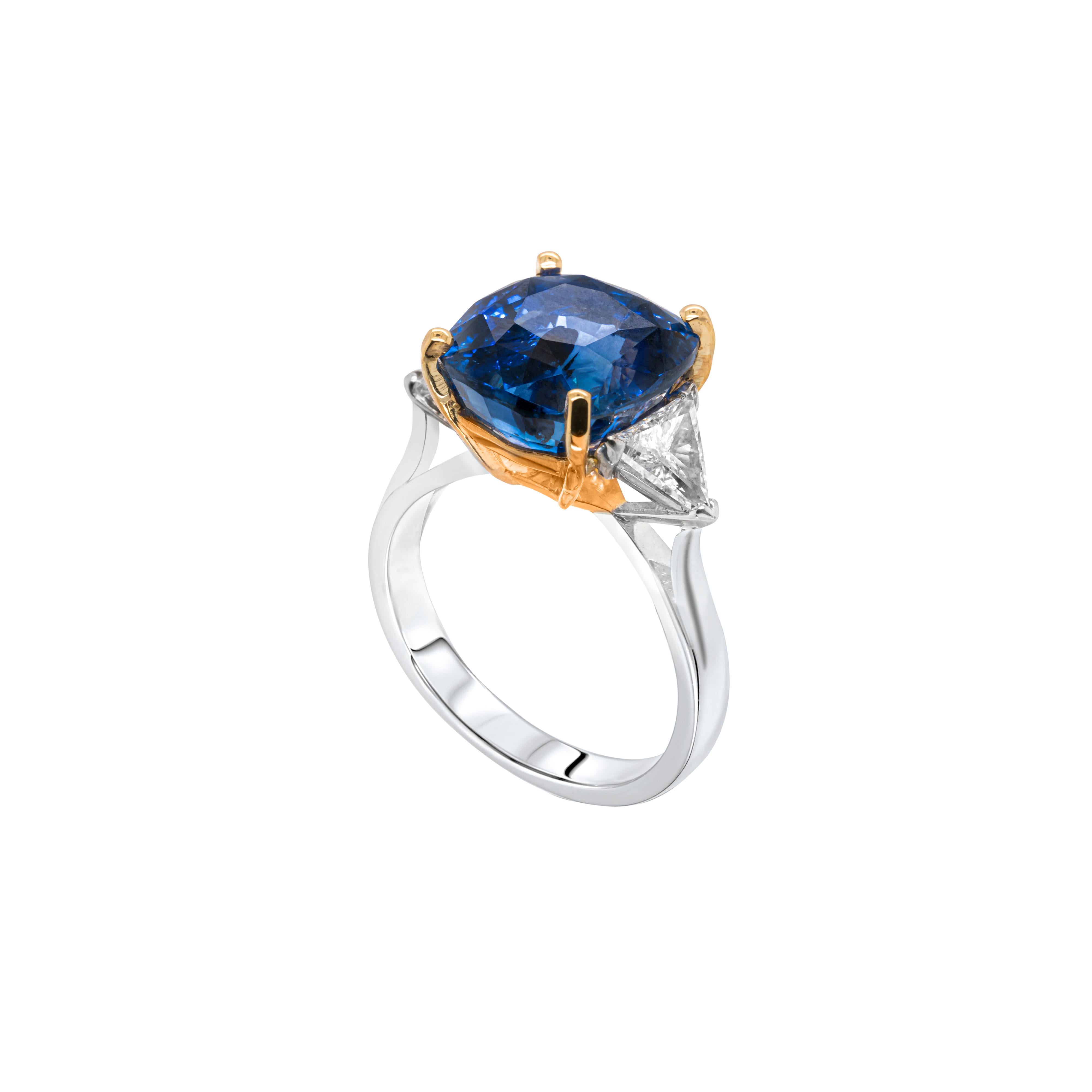 This stunning three stone engagement ring features a cushion cut blue sapphire weighing 9.73 carats mounted in a four claw, 18ct yellow gold setting. The gemstone is perfectly accompanied by a trillion cut diamond on either side with a combined