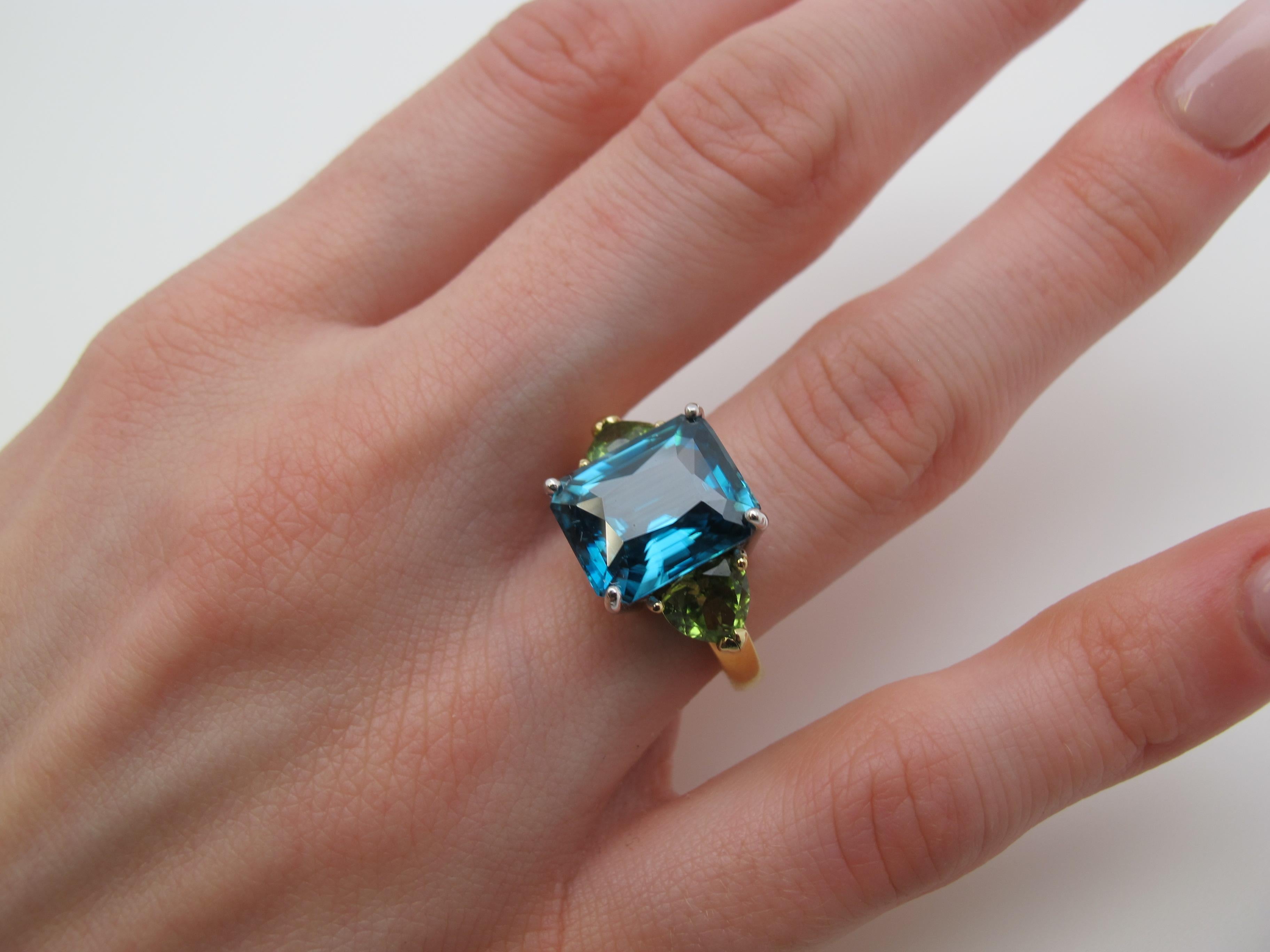 Neon turquoise blue (the color of Windex!) is the color of the beautiful, emerald-cut zircon featured in this ring. It is complemented by trillion-cut peridot side stones in a happy marriage of colors. All our stones are truly gems, possessing fine