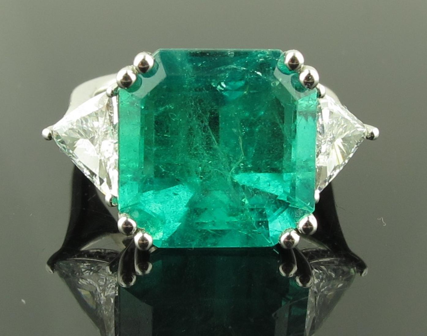 A 9.76 Square Cut center Emerald with 2 0.59 carat Trillion cut diamonds on the sides with 24 round brilliant cut diamonds surrounding stone.  Set in Platinum.  Ring size 6,
