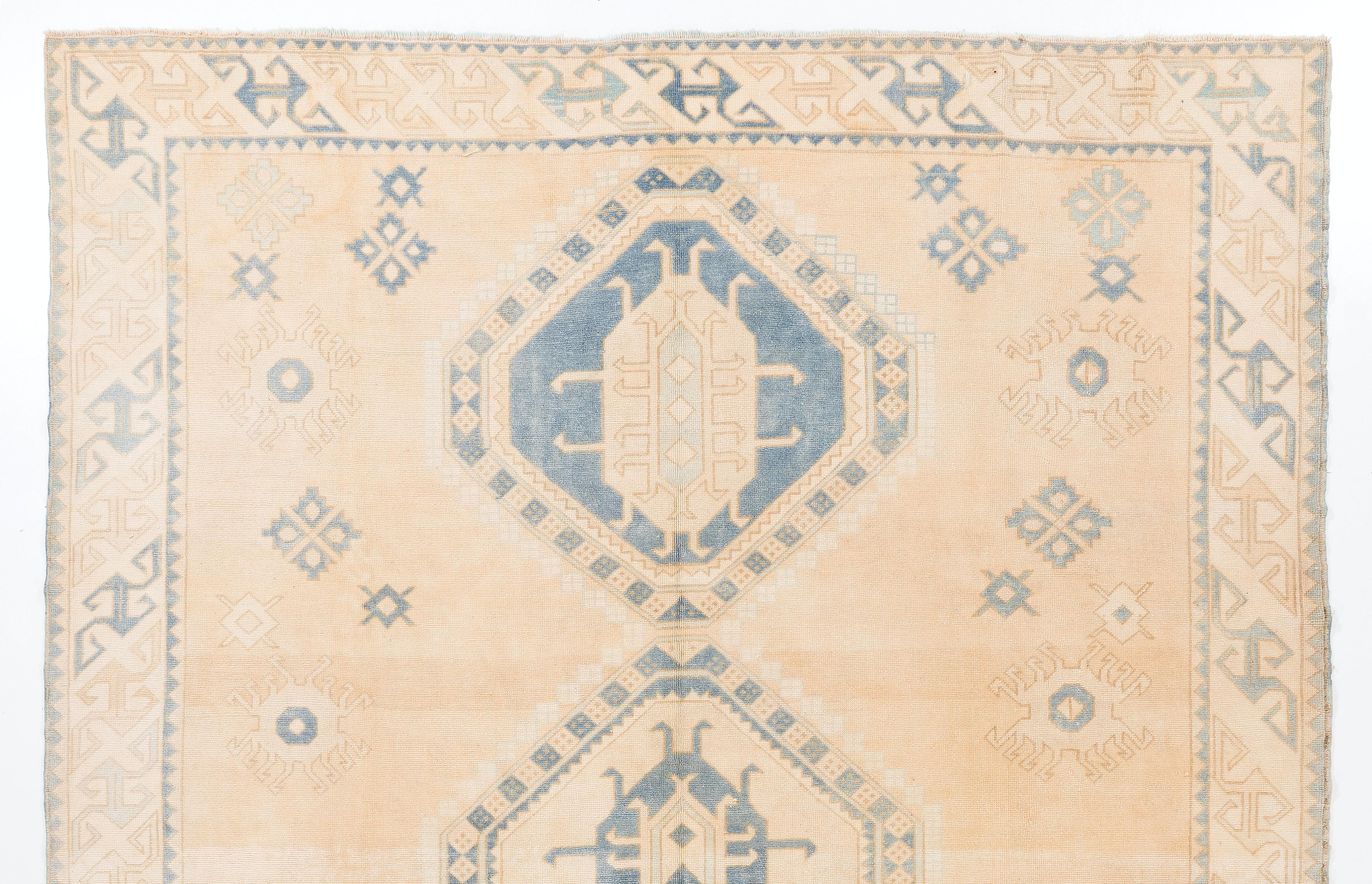 A vintage handmade central Anatolian rug with a bold design of three linked geometric medallions and depictions of some tribal motifs such as burdocks in the field and running water in the border in soft, muted  shades of coral pink and blue. It is