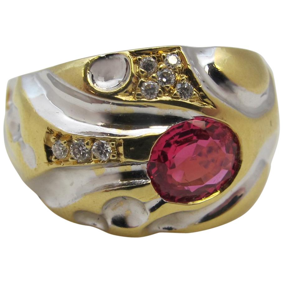 A fiery, brilliant, pinkish-red spinel is set with round brilliant cut diamonds in this wide, domed band of 18 karat white and yellow gold. The gold work has a retro feel with fun swirls and spheres, but the color combination adds a decidedly modern