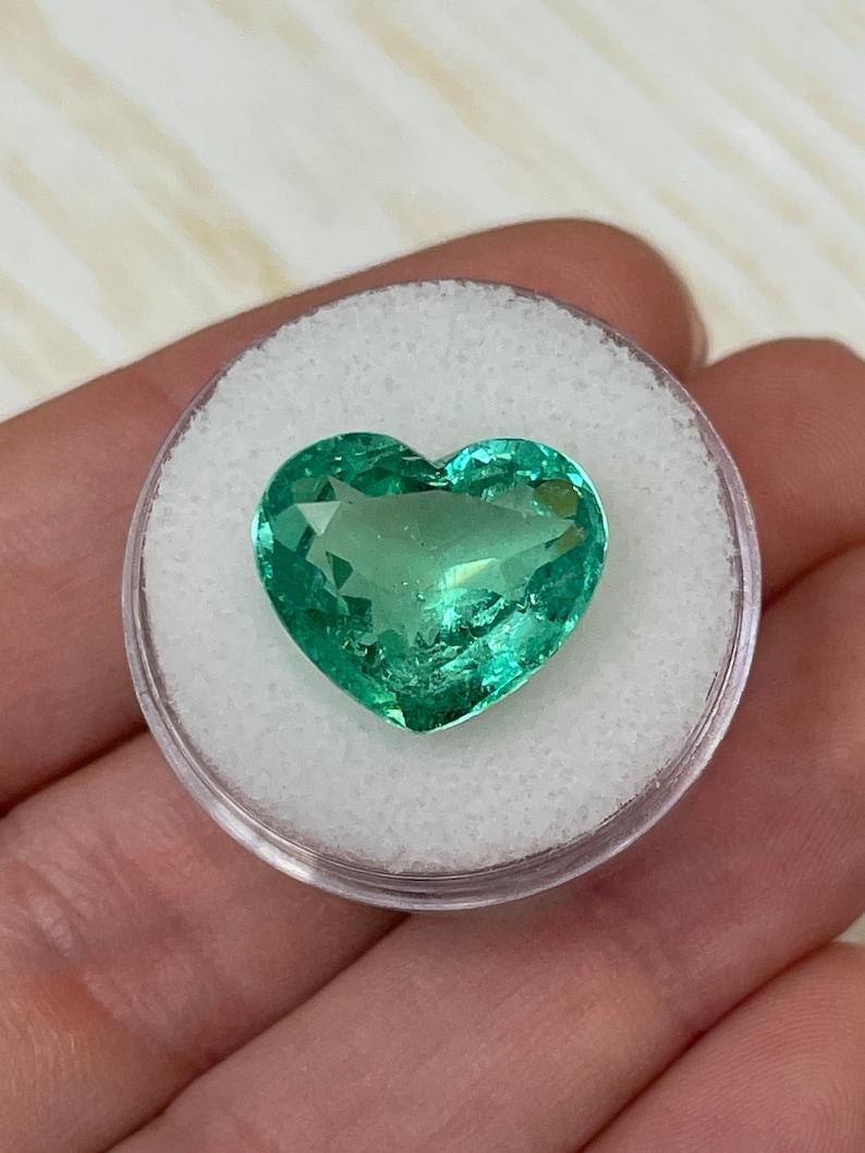 Stone: Emerald
Weight: 9.84-carats
Shape: Heart Cut
Clarity: Transparent
Luster: Very Good
Color: Medium Yellowish Green
Measurements: 13.29mm x 15.68mm x 8.10mm
Geographic Origin: Colombia
Treatment: Natural, Oiling

Comments: Due to their growth
