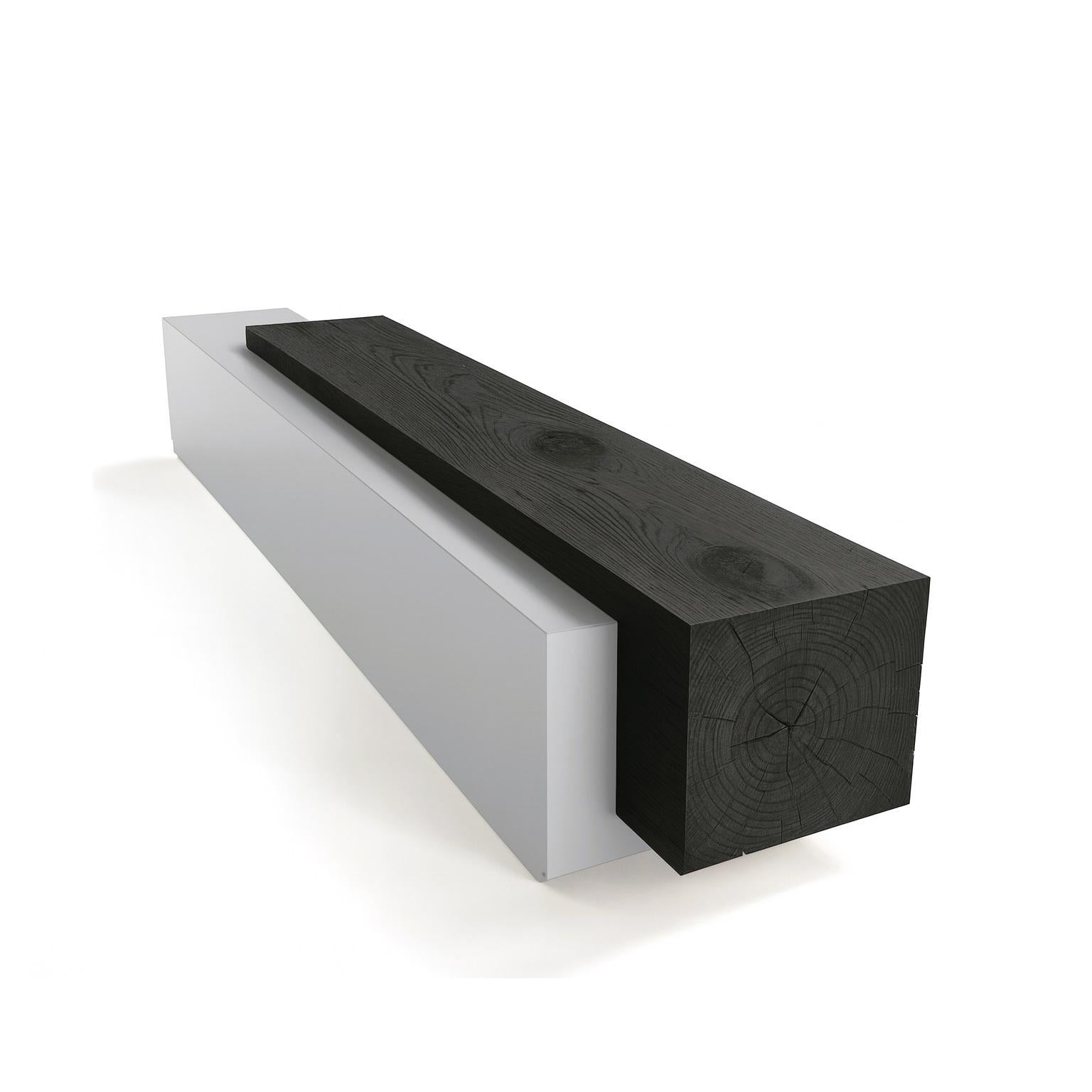 This sculptural bench is a striking composition of two integrated parallelepipeds, designed to evoke the image of an object and its shadow. It is crafted from two distinct materials: a solid, squared block of scented cedarwood is seamlessly joined