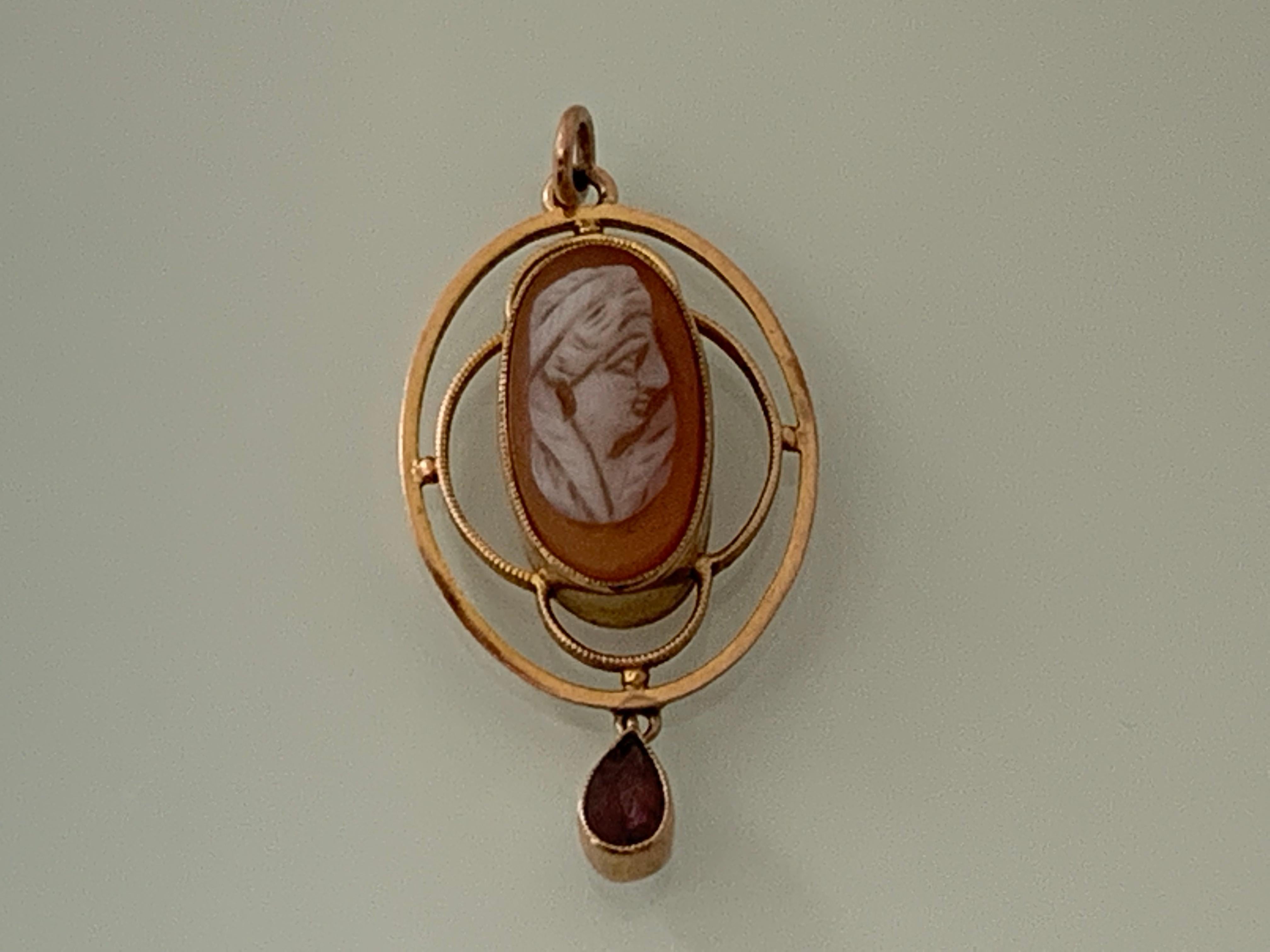 9ct Gold Italian Antique Cameo Pendant 
Hand carved cameo shell with a darker than usual background
enhanced by the setting which allows light to transcend through
with a dangling red teardrop gem that has faceted cut
Art Deco Era 
The cameo has a