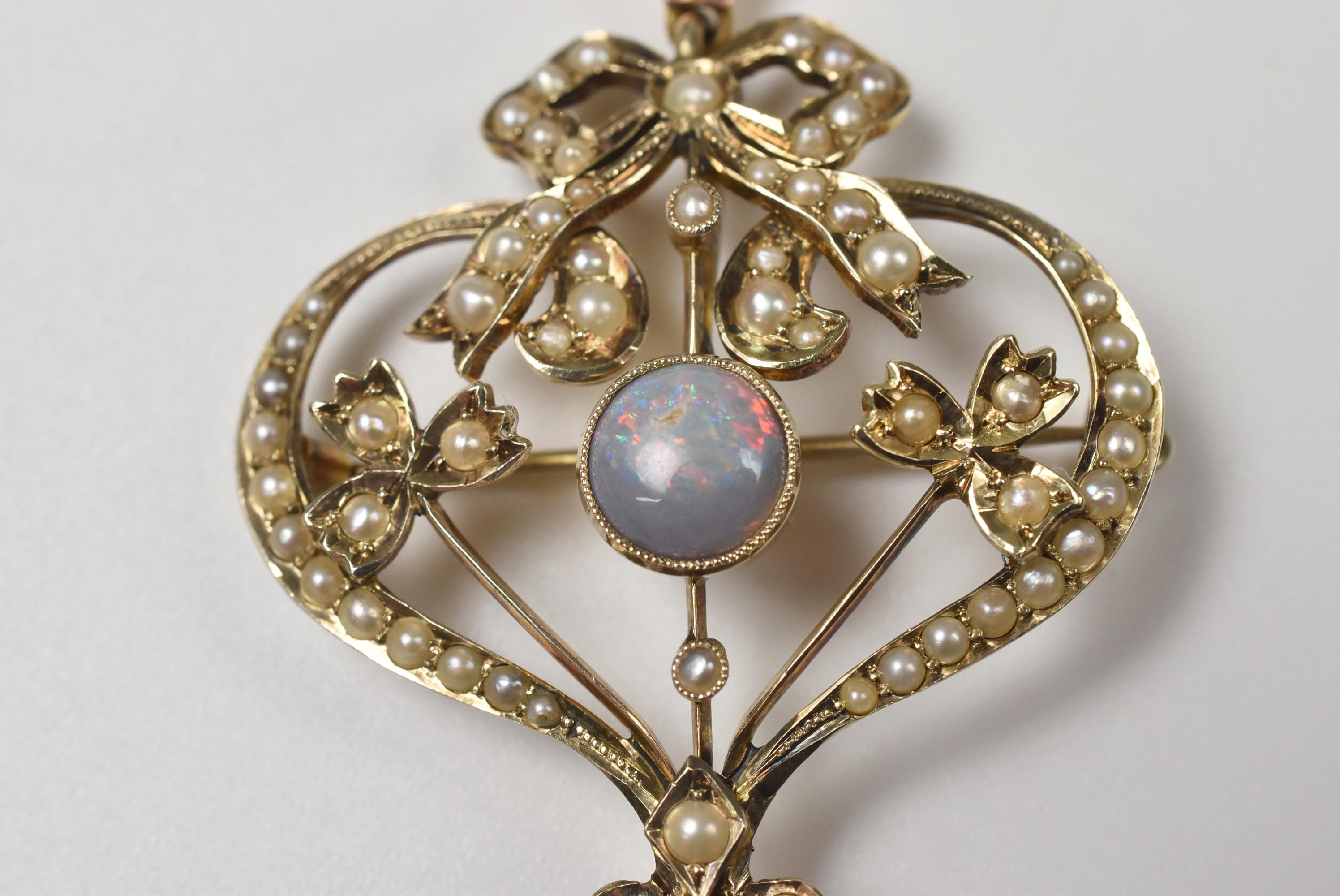 Heart shaped 9-karat gold Edwardian pendant or brooch. Central opal and an opal dangle at the bottom, surrounded by seed pearl bow, and flowers accents. Measures: 2 1/4