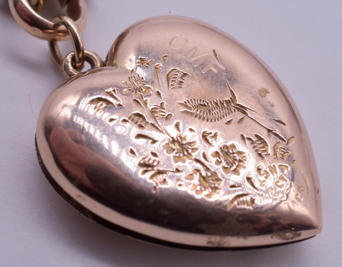 Antique 9K heart shaped locket with stylized and charming designs on each side; one with a tall wildflower languishing and a heron or a crane foraging nearby. The other side shows what appears to be a bird carrying a bouquet of some sort. There is a