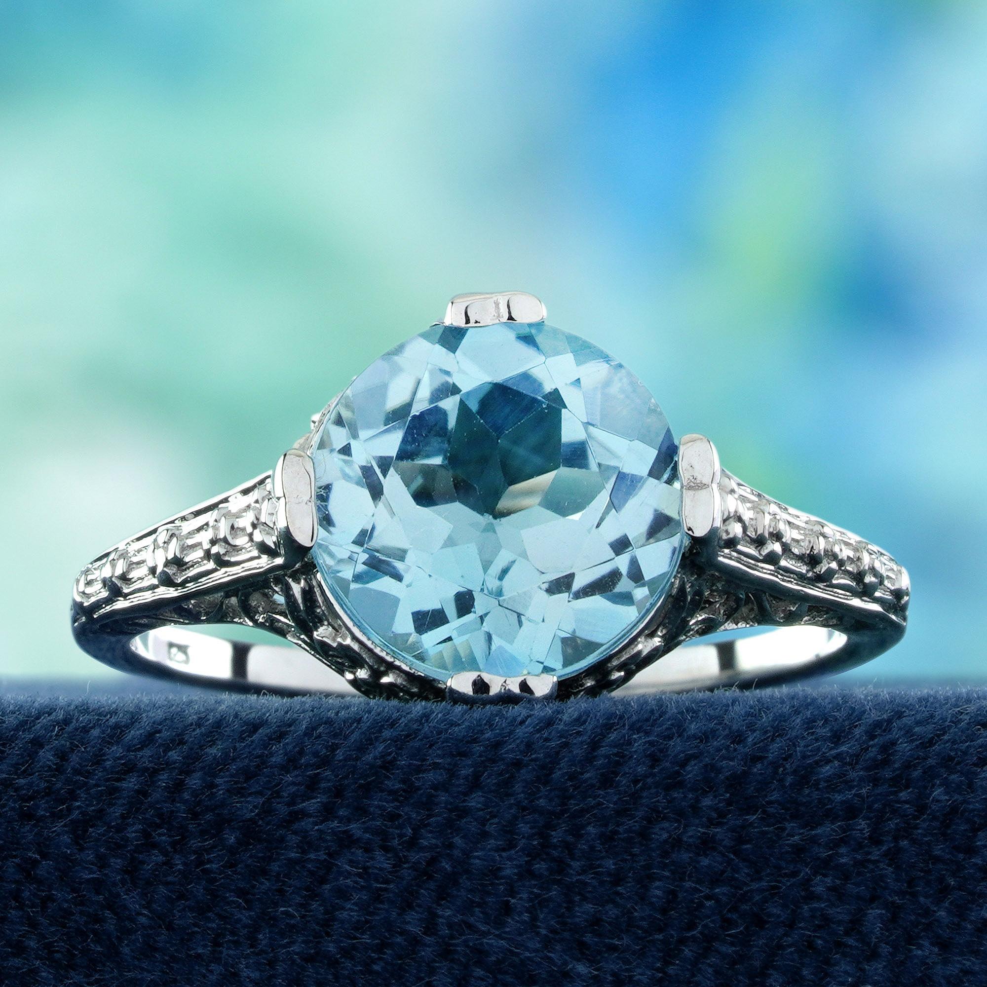 Il topazio blu rotondo brillante è incastonato in una classica montatura a griffe. Le spalle presentano delicati motivi floreali in filigrana, che aggiungono un fascino vintage e artistico al design. Questo anello bilancia magnificamente il blu
