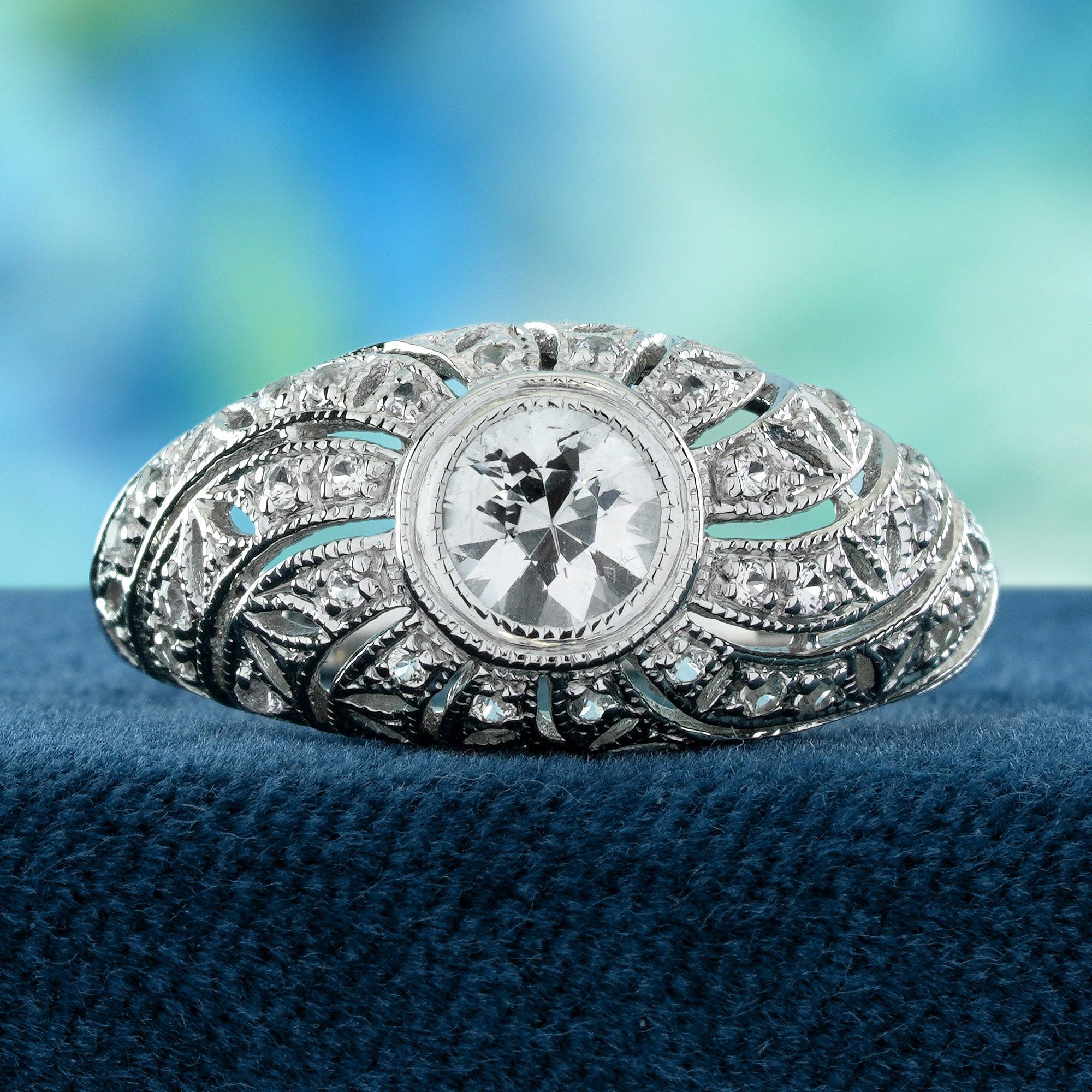 In seinem Zentrum sitzt ein runder weißer Saphir, der pure Eleganz und Klarheit ausstrahlt. Die vom Vintage-Stil inspirierte Fassung zeichnet sich durch filigrane Details aus, die das natürliche Funkeln des Steins betonen. Dieser Ring ist perfekt,