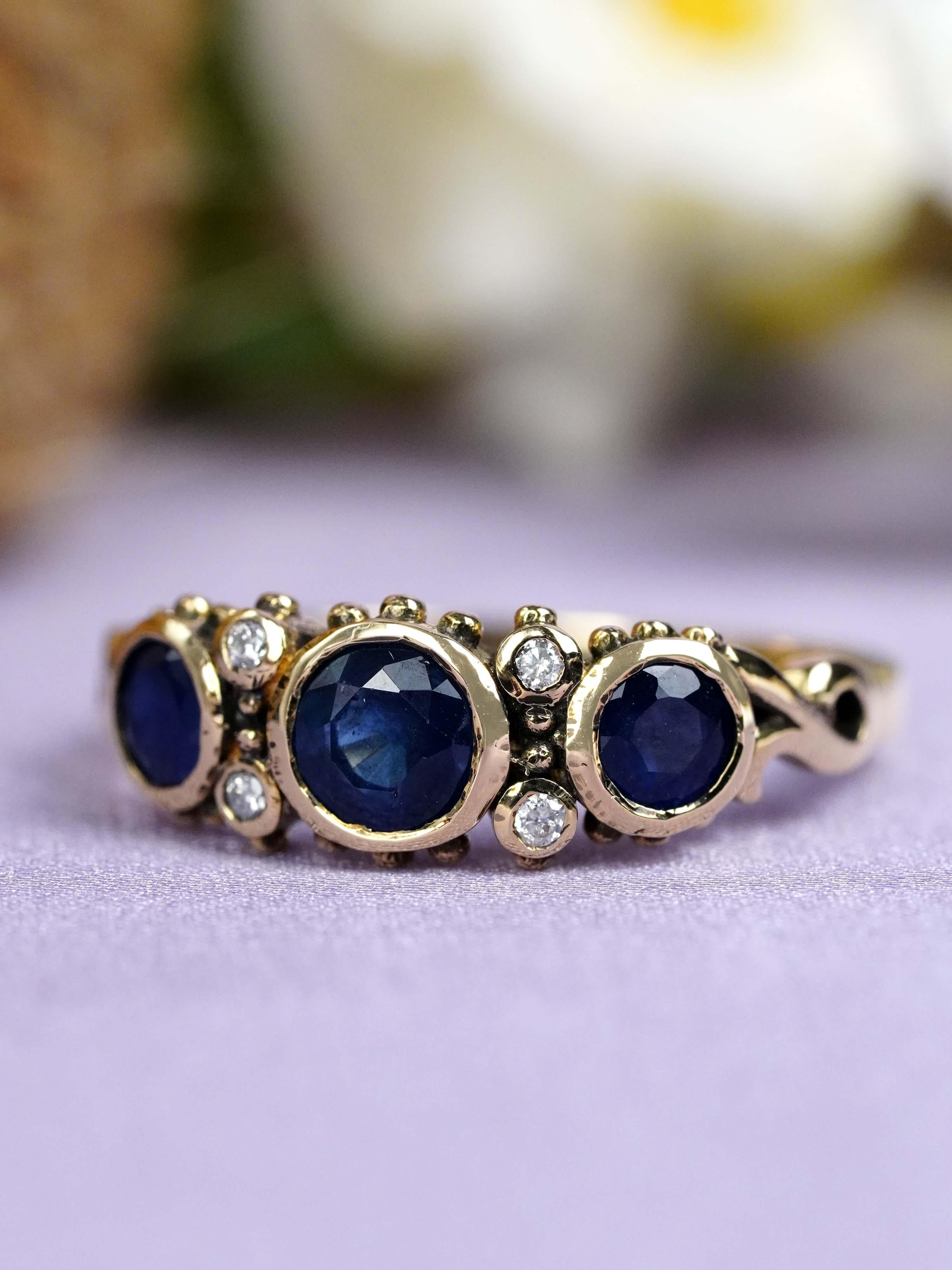 Dieser dreiteilige Ring im Vintage-Stil besteht aus runden blauen Saphiren, die in einer anmutigen Reihe gefasst sind. Zwischen jedem Saphir sorgt ein funkelnder Diamant für Brillanz und einen eleganten Kontrast. Die Kombination schafft einen