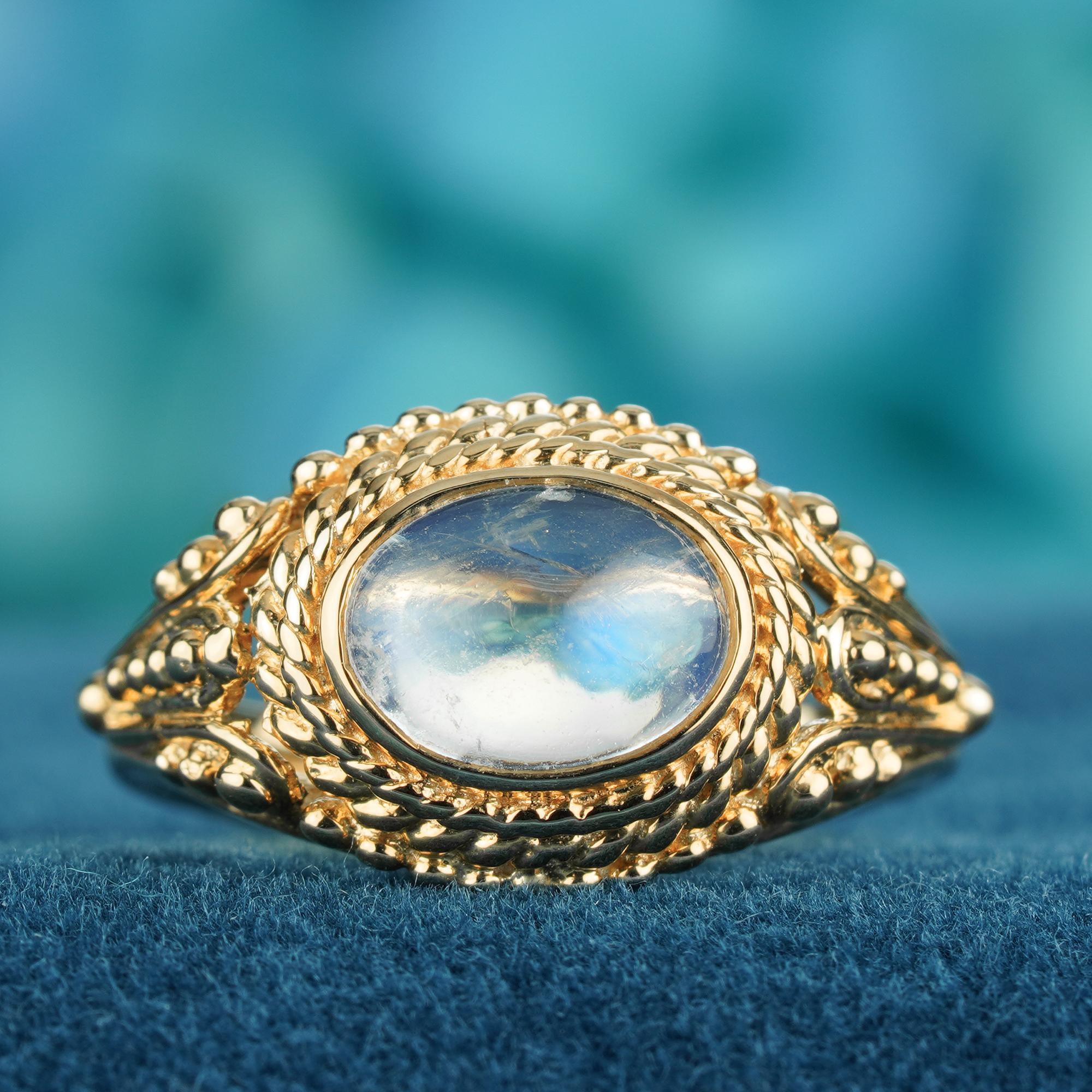 A natural cabochon moonstone, glowing with a soft, mystical shimmer. The smooth, domed stone is beautifully set to catch the light from every angle. Intricate vintage-inspired detailing on the band adds timeless elegance and delicate charm. A