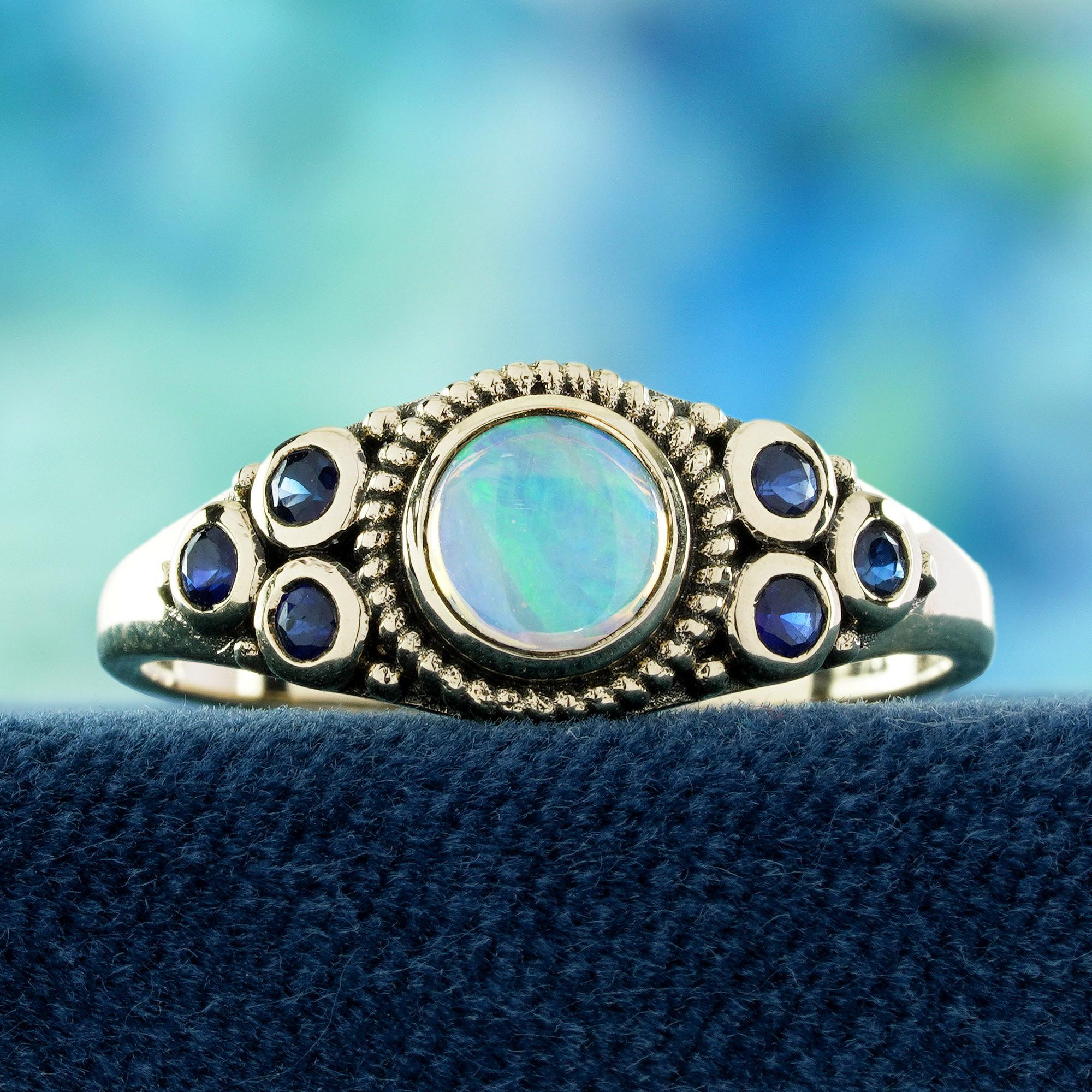 Ein leuchtender, runder, natürlicher Opal ist sicher in eine glatte Lünette gefasst. Der Opal wird auf jeder Seite von drei tiefblauen Saphiren flankiert, wodurch ein ausgewogenes und elegantes Design entsteht. Die Kombination des schillernden Opals