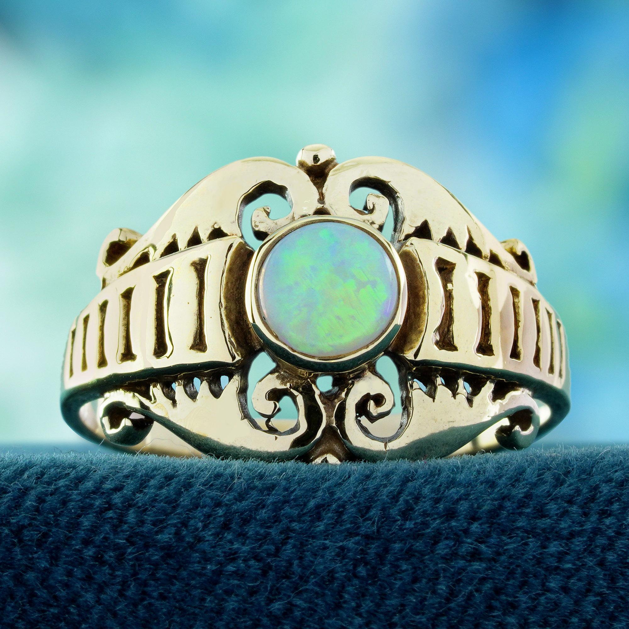 In der Mitte befindet sich ein leuchtender, runder Opal, der sanfte, schillernde Farbtöne ausstrahlt, die sich bei jedem Blick verändern. Zarte, filigrane Wirbelmotive zieren die Schultern und verleihen dem Vintage-Design einen romantischen, von der