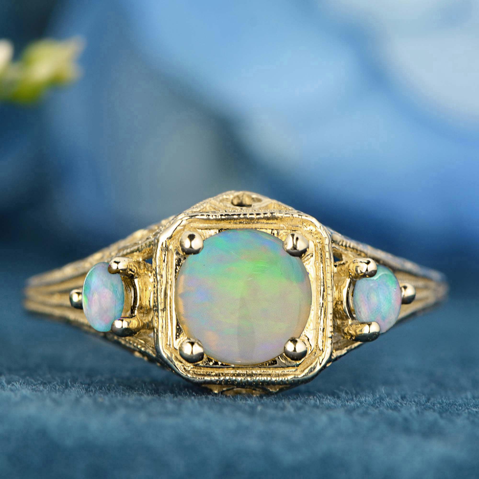 Three-stone ring features a radiant round natural opal prong-set at the center, showcasing its mesmerizing play of colors. Flanking the center stone are smaller opals on each side, seamlessly integrated into delicate filigree shoulders. The