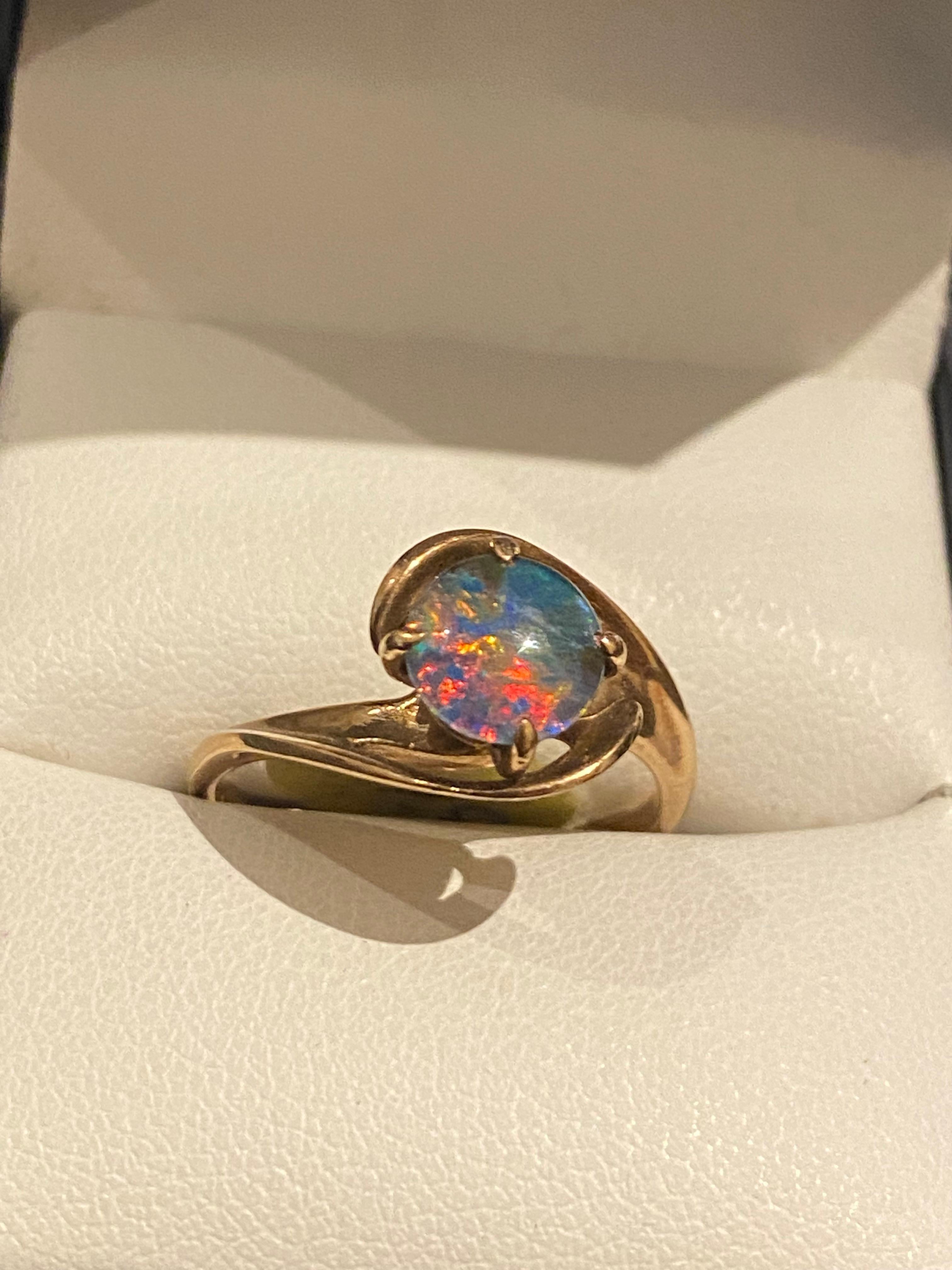 Bague vintage en or et opale de provenance australienne, 
serti au centre d'une opale double ronde 
de 7,5 mm - 8 mm environ. 
de la myriade de couleurs : 
rouge, orange, bleu, violet et jaune 
serti clos dans une monture by-pass
en or jaune 9K