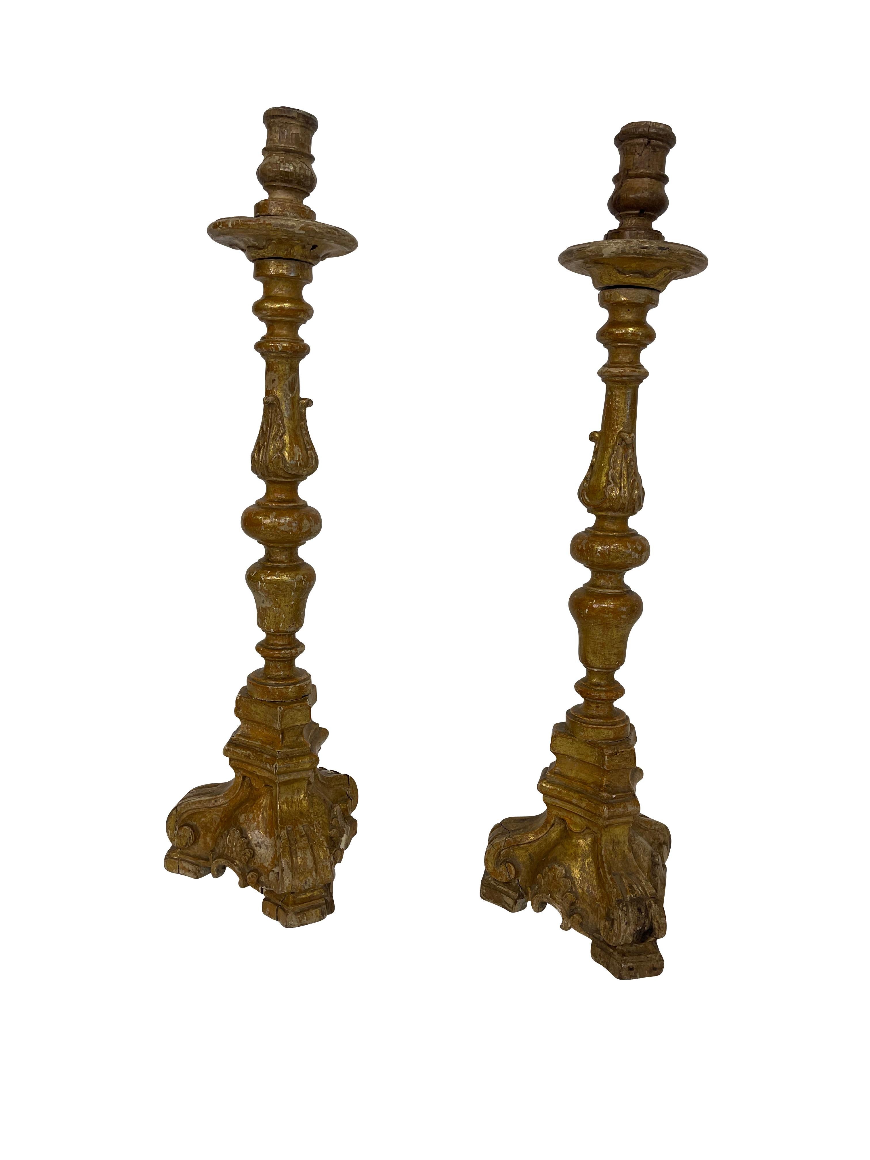 Pair of 19th century antique baroque Italian candlesticks, hand carved in giltwood with a lovely patina. Expertly hand carved on scrolled feet, these candlesticks stand over two feet tall and make a dramatic statement in any room of your house. They