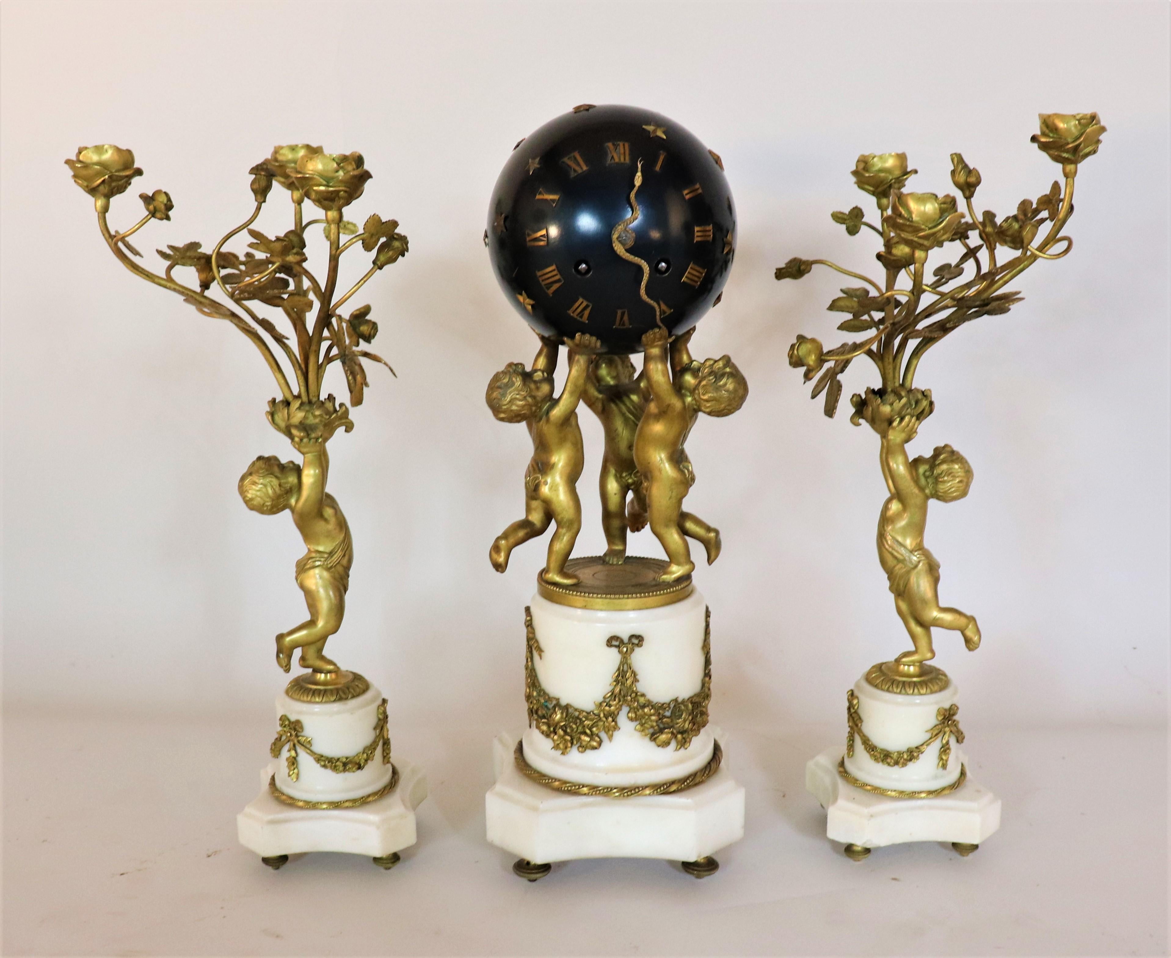 Circa 1890 French Jewel Escape Movement Bronze and Marble Three Piece Clock and Candle Garniture. The clock piece of this set features three bronze putti holding up a black spherical Roman numeral clock. It is what is called a 