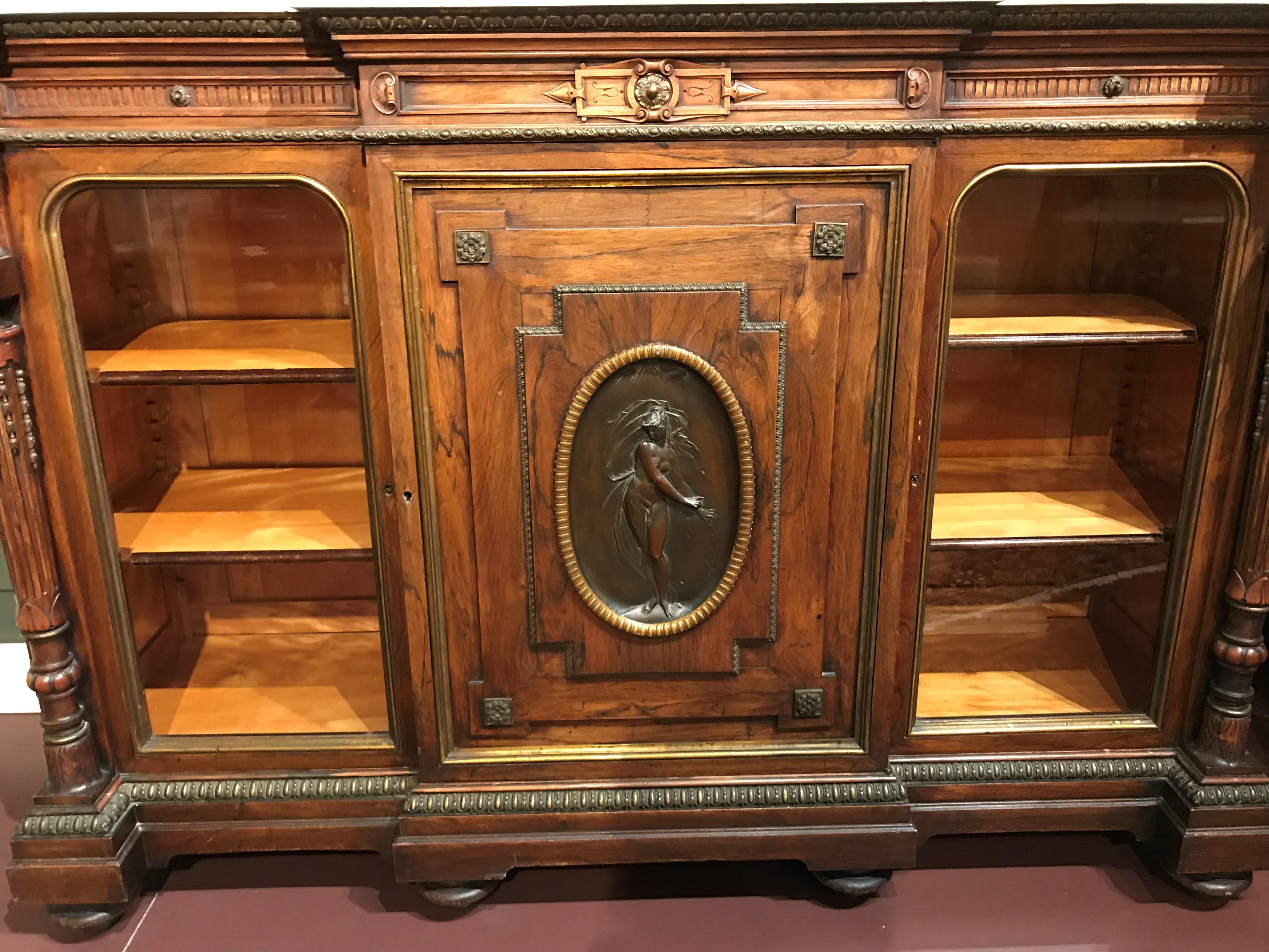 A 19th century rosewood credenza with conforming marble top surmounting a case with foliate decorated ormolu, a large central paneled door adorned with a oval bronze plaque of a semi-nude classical female figure and corner rosettes, opening to a