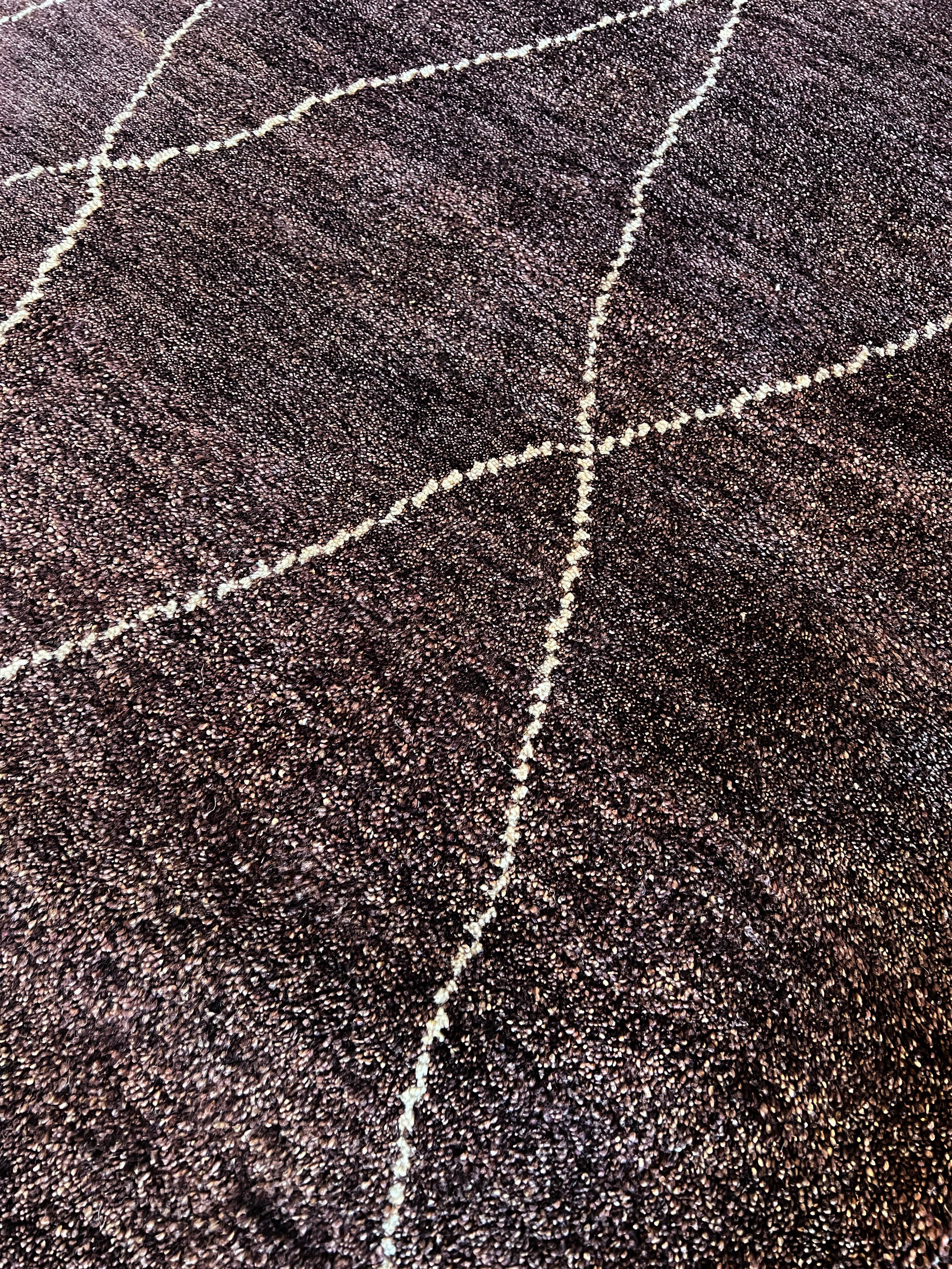 Bringen Sie einen Hauch von Eleganz in Ihr Zuhause mit unserem 9'x12' mauvebraunen marokkanisch inspirierten Teppich. Er wird in Indien aus reiner Wolle handgeknüpft und hat eine weiße Akzentlinie, die ihm einen klassischen Touch verleiht. Erleben