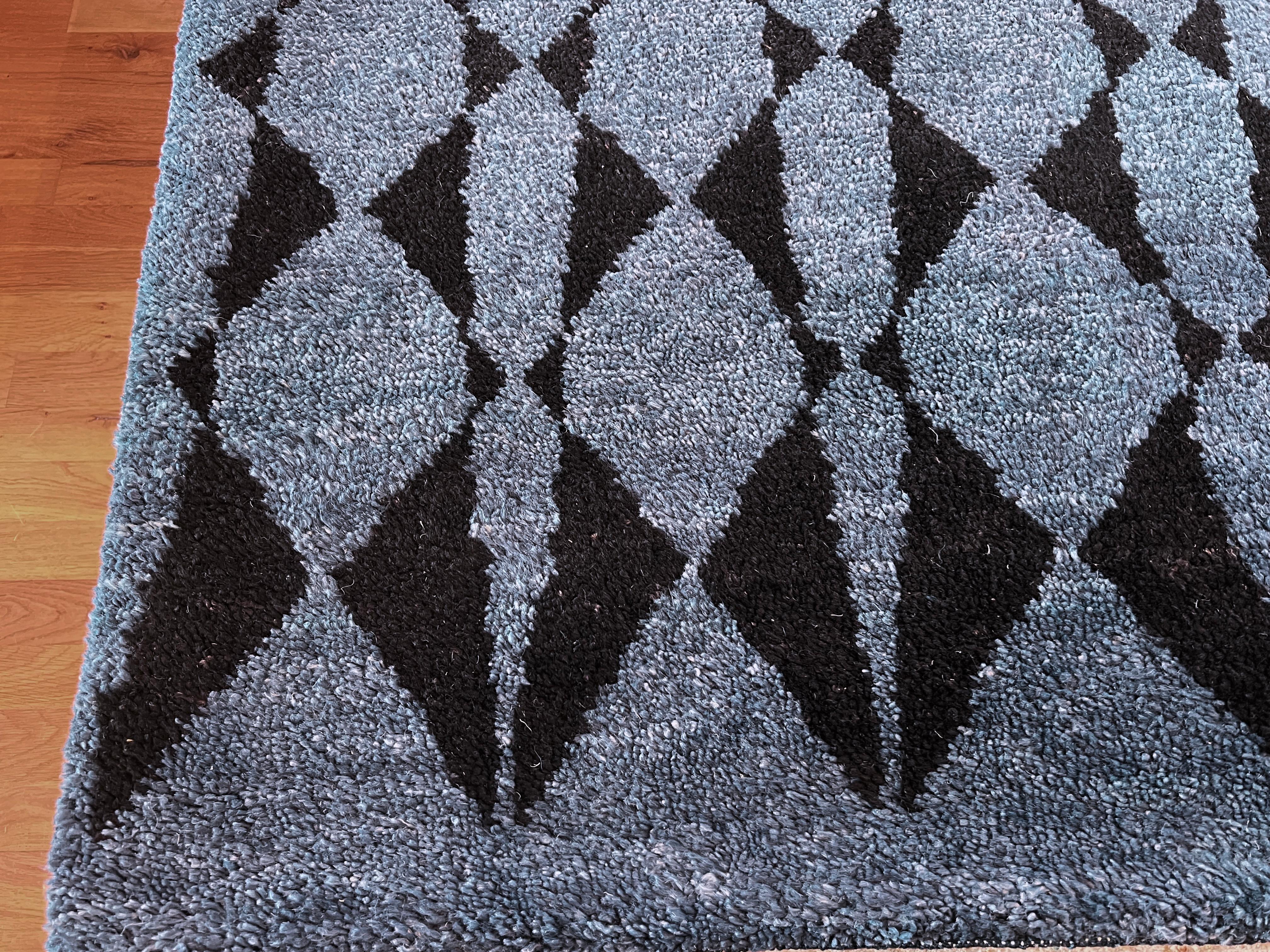 Verleihen Sie Ihrem Zuhause mit unserem marokkanischen Teppich 9'x12' einen Hauch von modernem Stammesstil. Der leuchtend marineblaue Hintergrund und die schwarzen Rauten setzen in jedem Raum einen Akzent. Dieser weiche und strapazierfähige Teppich