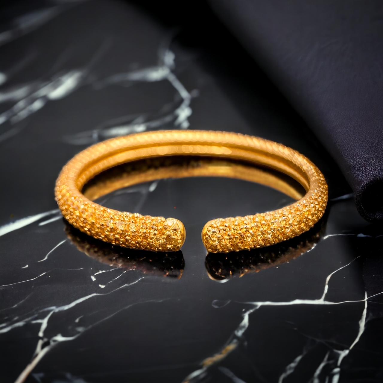 A pavé fancy yellow diamond sprung bangle in 18ct yellow gold; With approximately 12cts of diamonds of strong yellow hue. Bangle width 9mm. External circumference: 5.7mm. Internal circumference: 5mm. Marked 750 18K. Price 32,000£. Item is in very