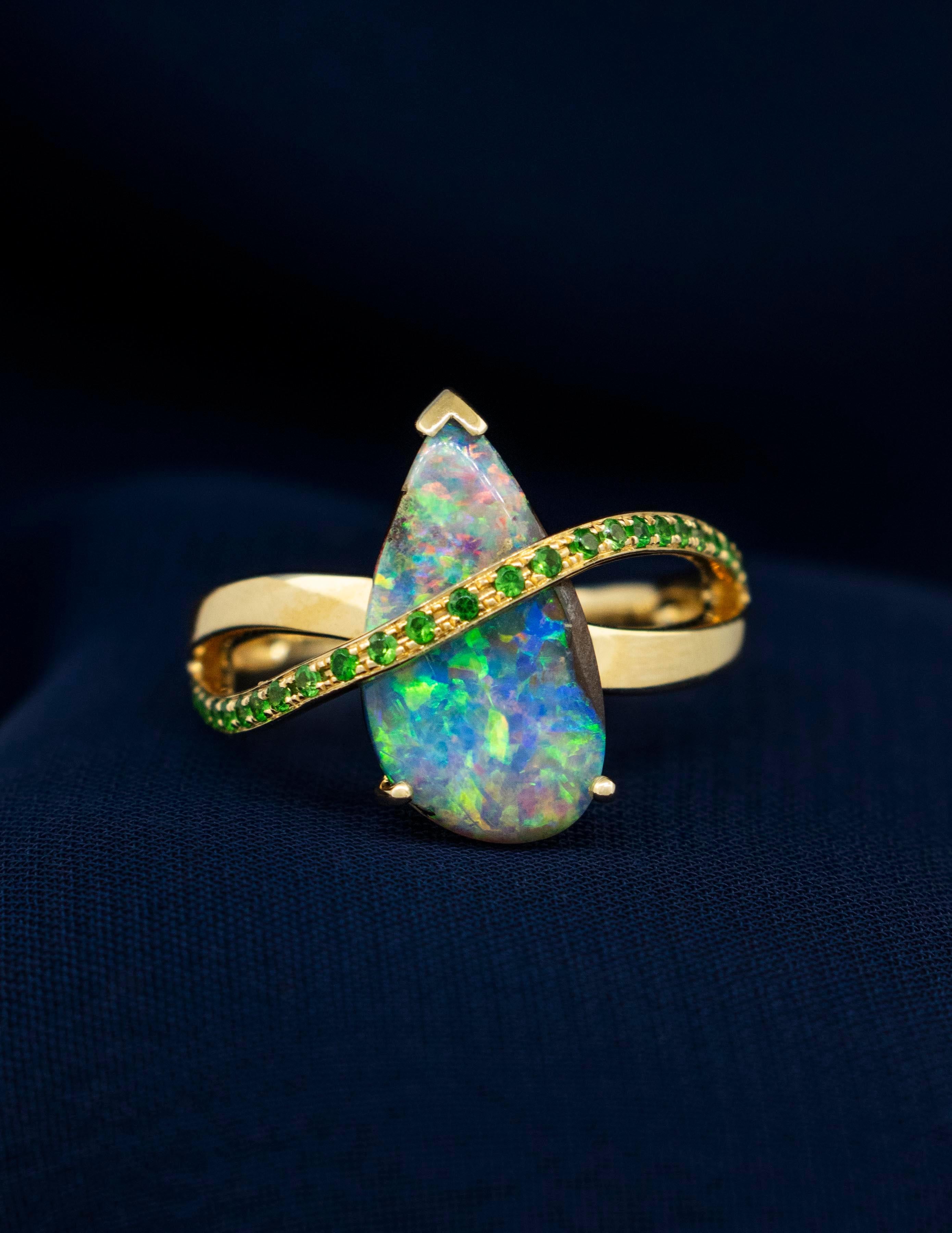 A 14K Yellow Gold Contemporary Style Ring with Black Opal and Tsavorite Garnets. The Australian Black Opal is a natural, earth mined stone with scintillating shades of Green, Blue, Gold and Fiery Reds. The Pear Shape Opal weighs approx. 2.38 carats.