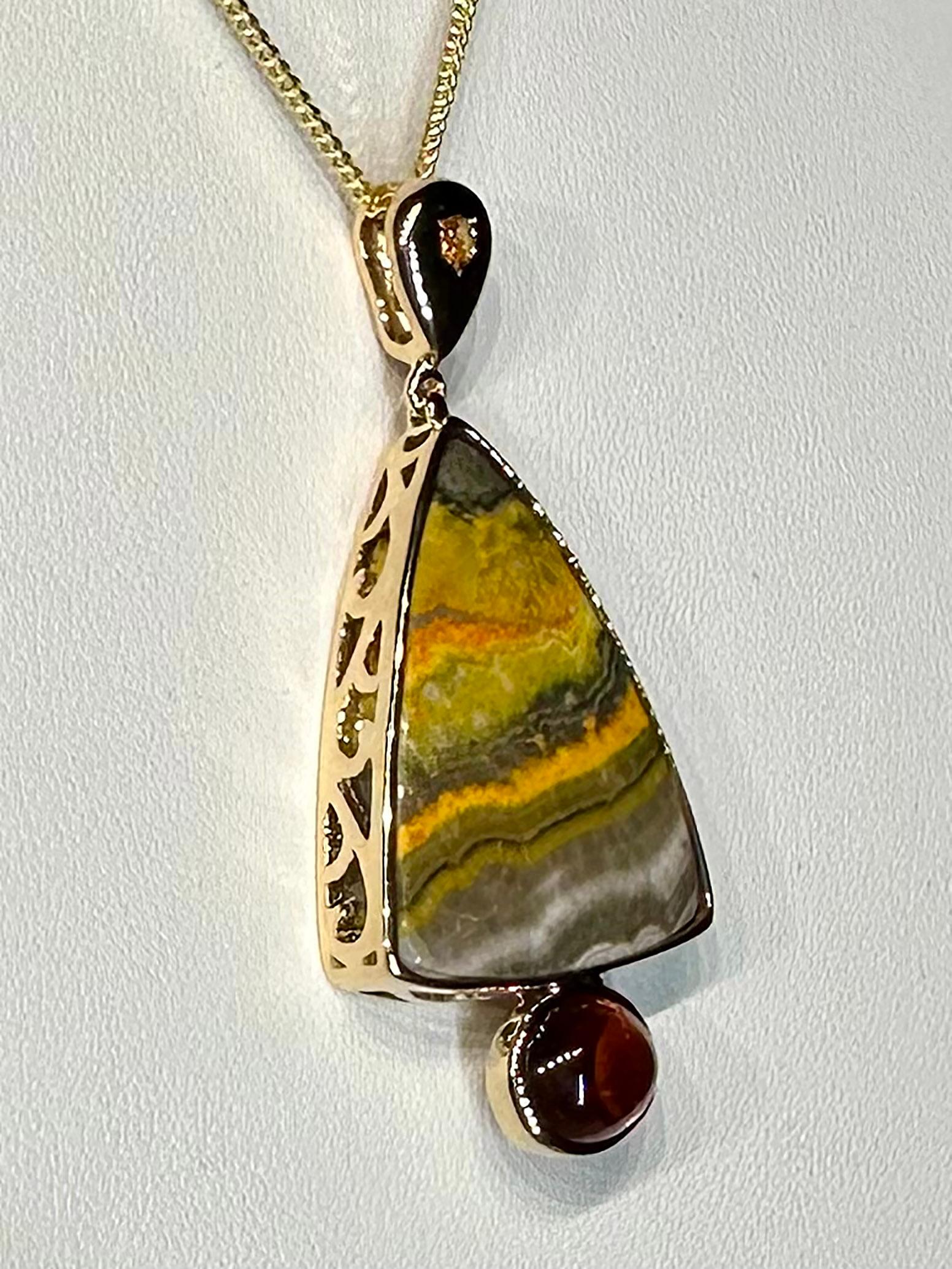 A 14kt Yellow Gold Pendant with Sapphire, Jasper & a Spessartine Garnet Cabochon. An exquisite 14kt Yellow Gold Pendant featuring a Sapphire, Jasper, and a Spessartine Garnet Cabochon. Elevate your style with this stunning piece of fine