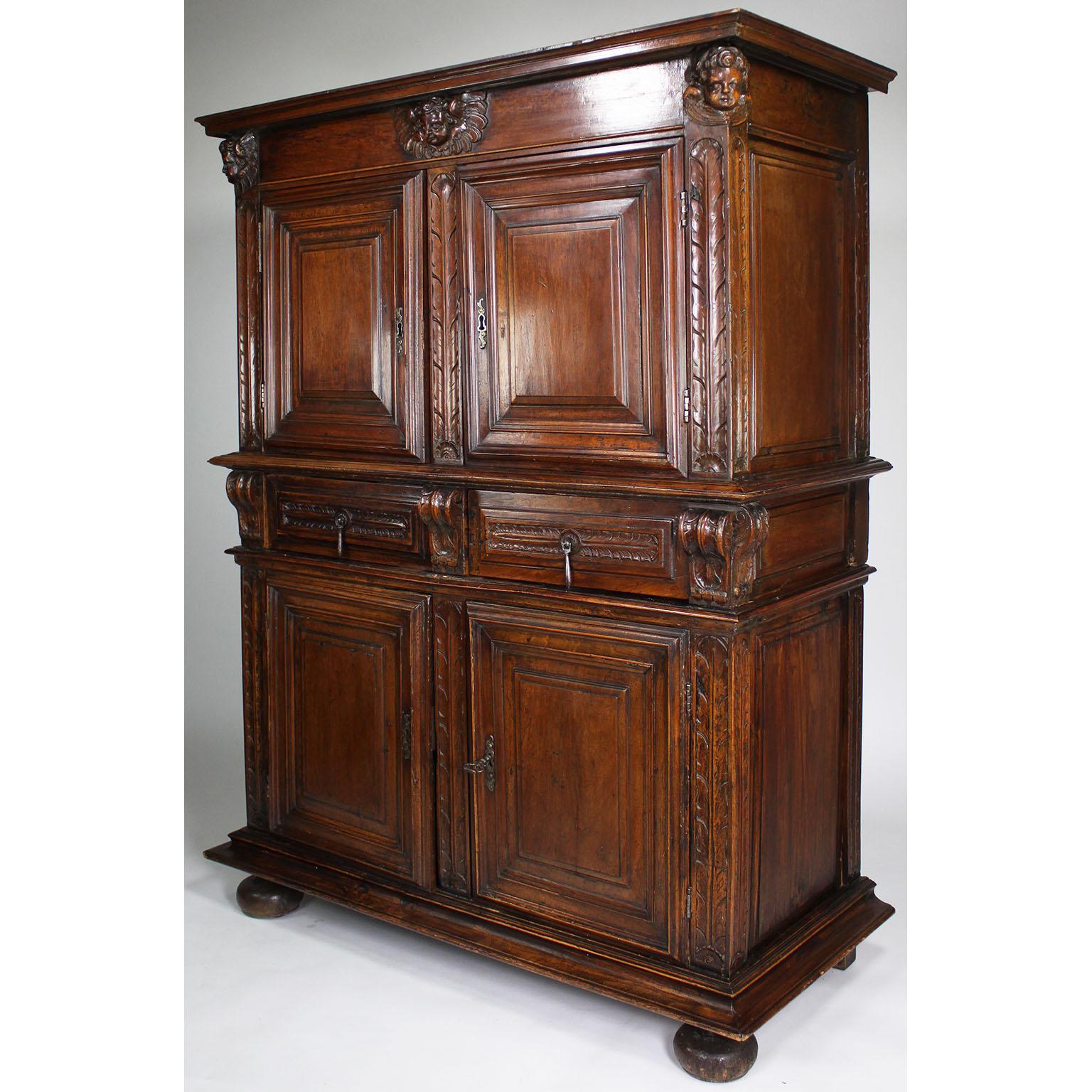 A 17th-18th Century French/Italian Renaissance Walnut Figural Carved Credenza Cabinet or Cupboard. The two-part cabinet with a pair of upper coffered doors with metal key-hole hardware below carved figure of cherub-heads, the apron with a pair of