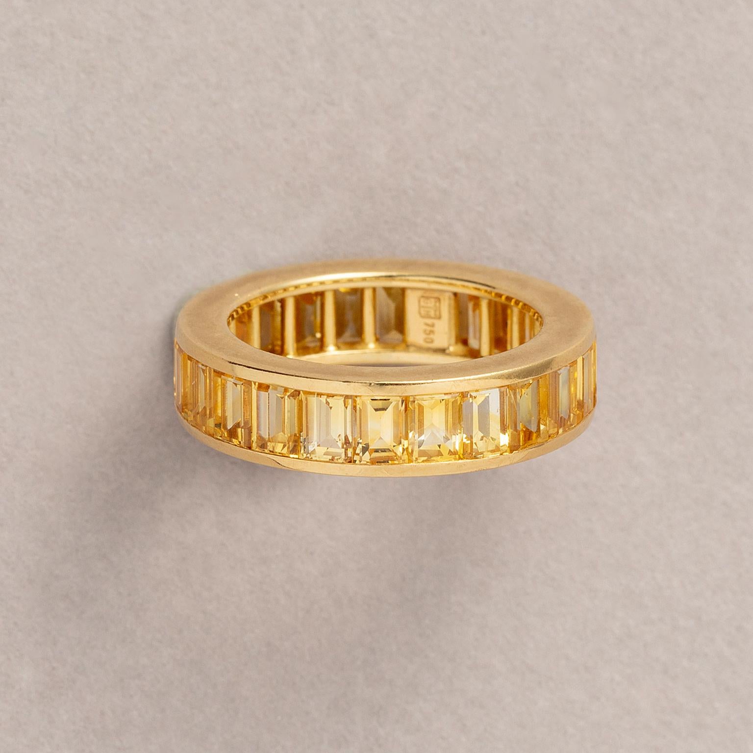 An 18 carat yellow gold eternity ring set with baguette cut yellow sapphires (app. 6.67 carats) vertically set in rails setting, signed with GH under hammer for Hemmerle, Münich. 

weight: 6.92 grams
ring size: 16.80 mm /  6 1/2 US
width: 5 mm