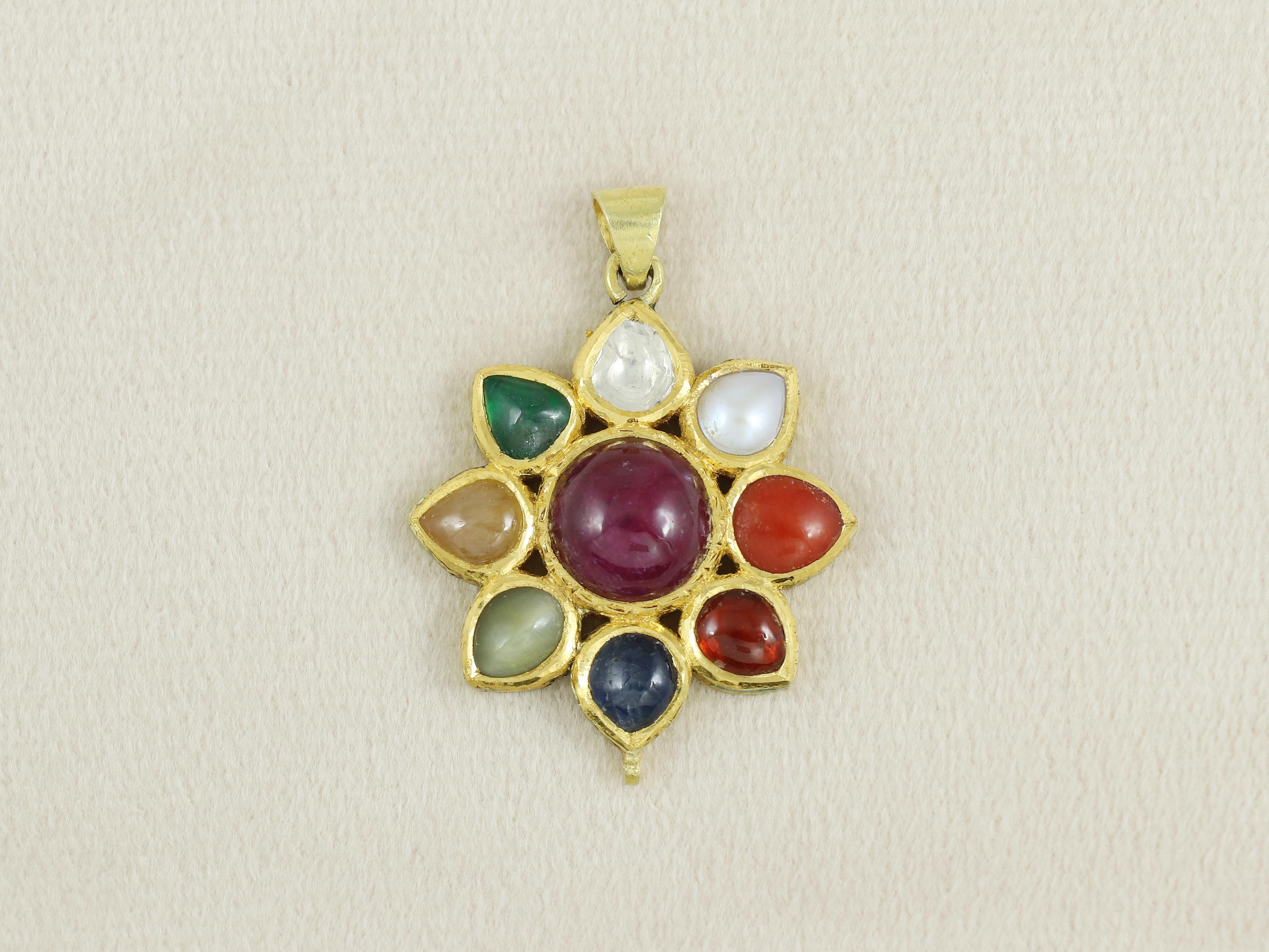 This 18K gold pendant is set with nine auspicious planetary gems (navratna) with a natural round ruby cabachon at the centre surrounded with - clockwise from top - diamond polki, pearl, coral, Hessonite garnet, blue sapphire, cat's eye, Yellow