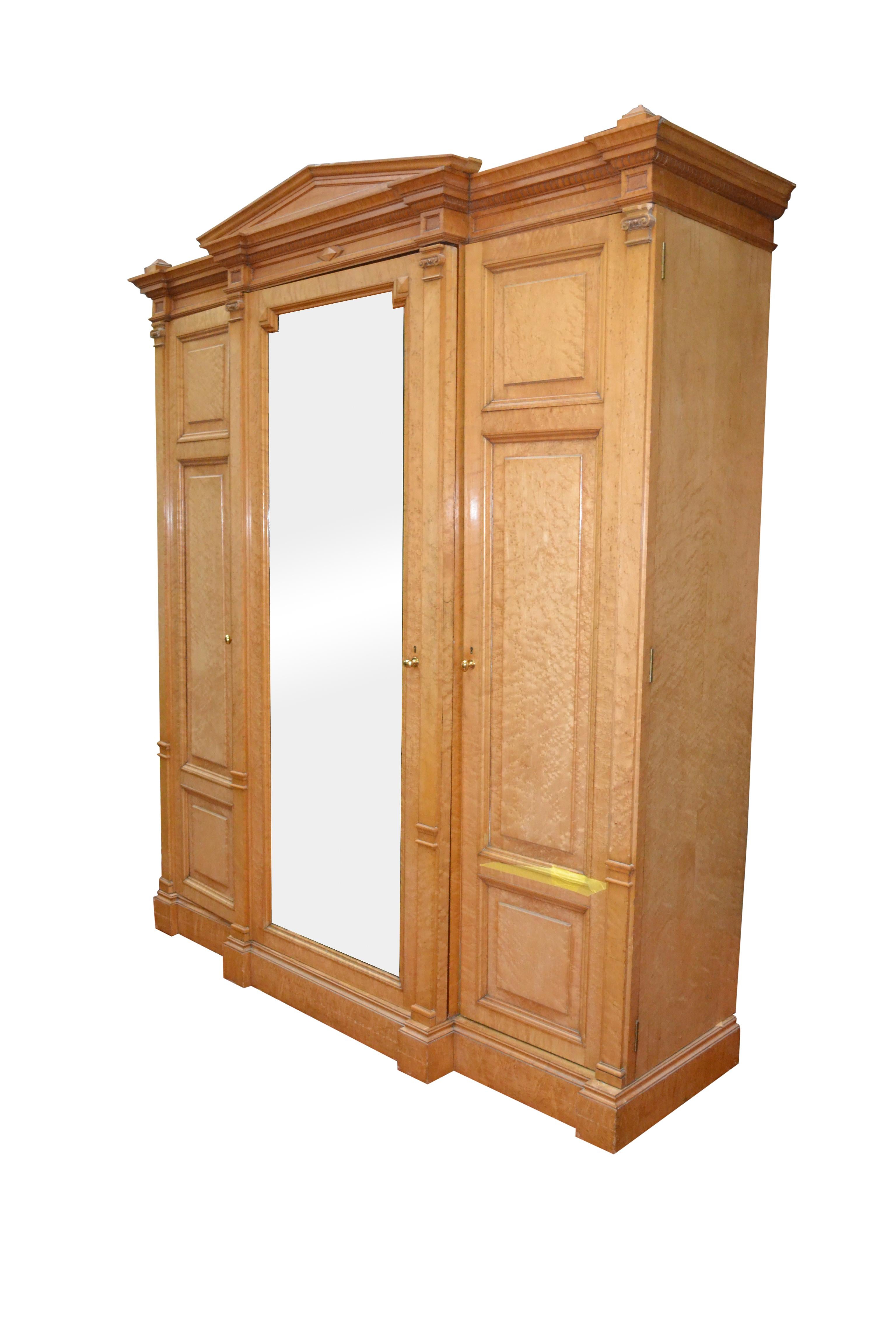 A mid-19th century American richly finished armoire in bird’s-eye maple of neoclassic architectural shape and proportions; the cabinet is in three sections framed by ionic pilasters, the middle section features a full length bevelled mirror below a